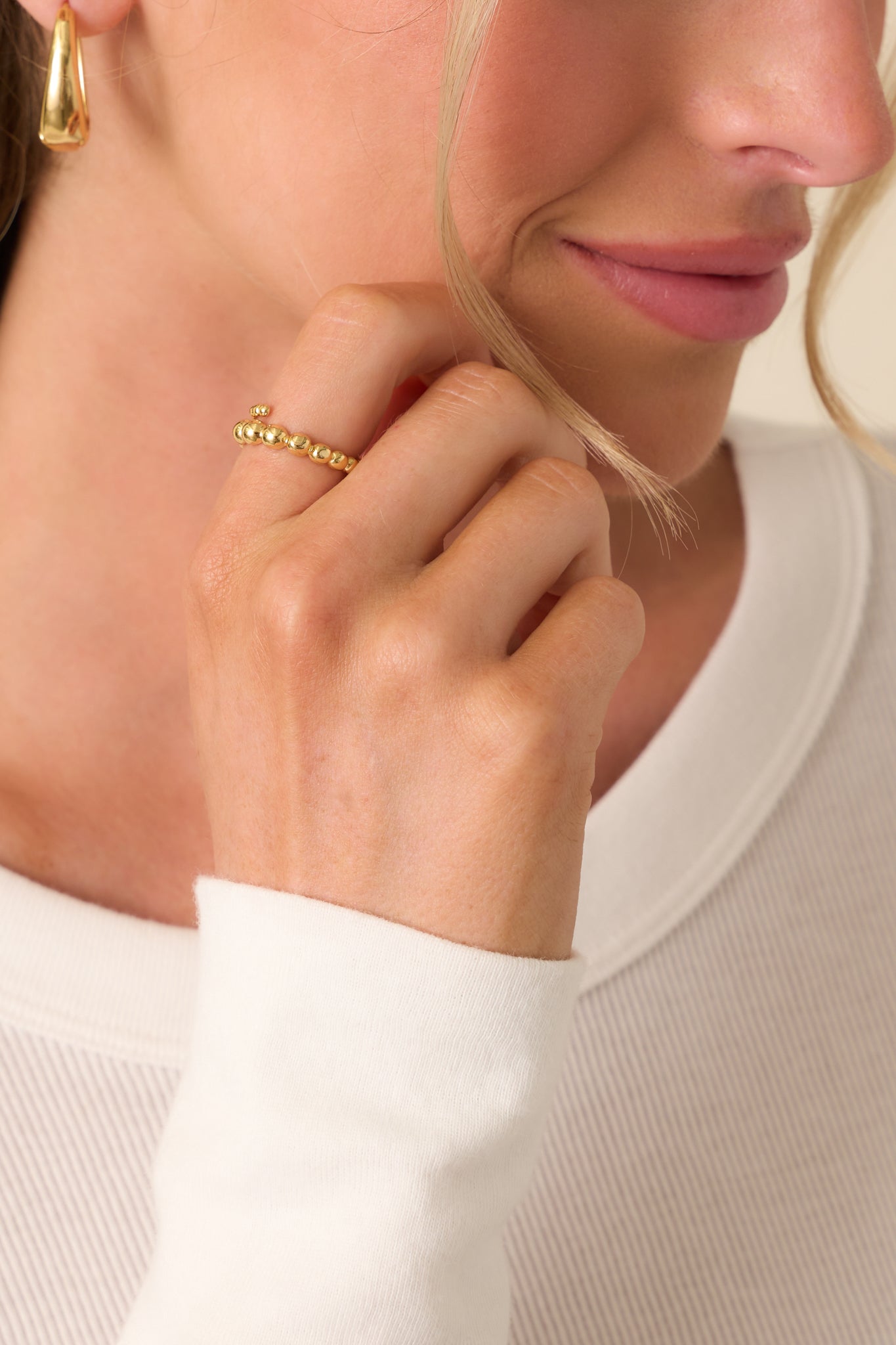 Close-up of the gold ring showing its open band and graduated ball detailing, wrapped gently around the finger.