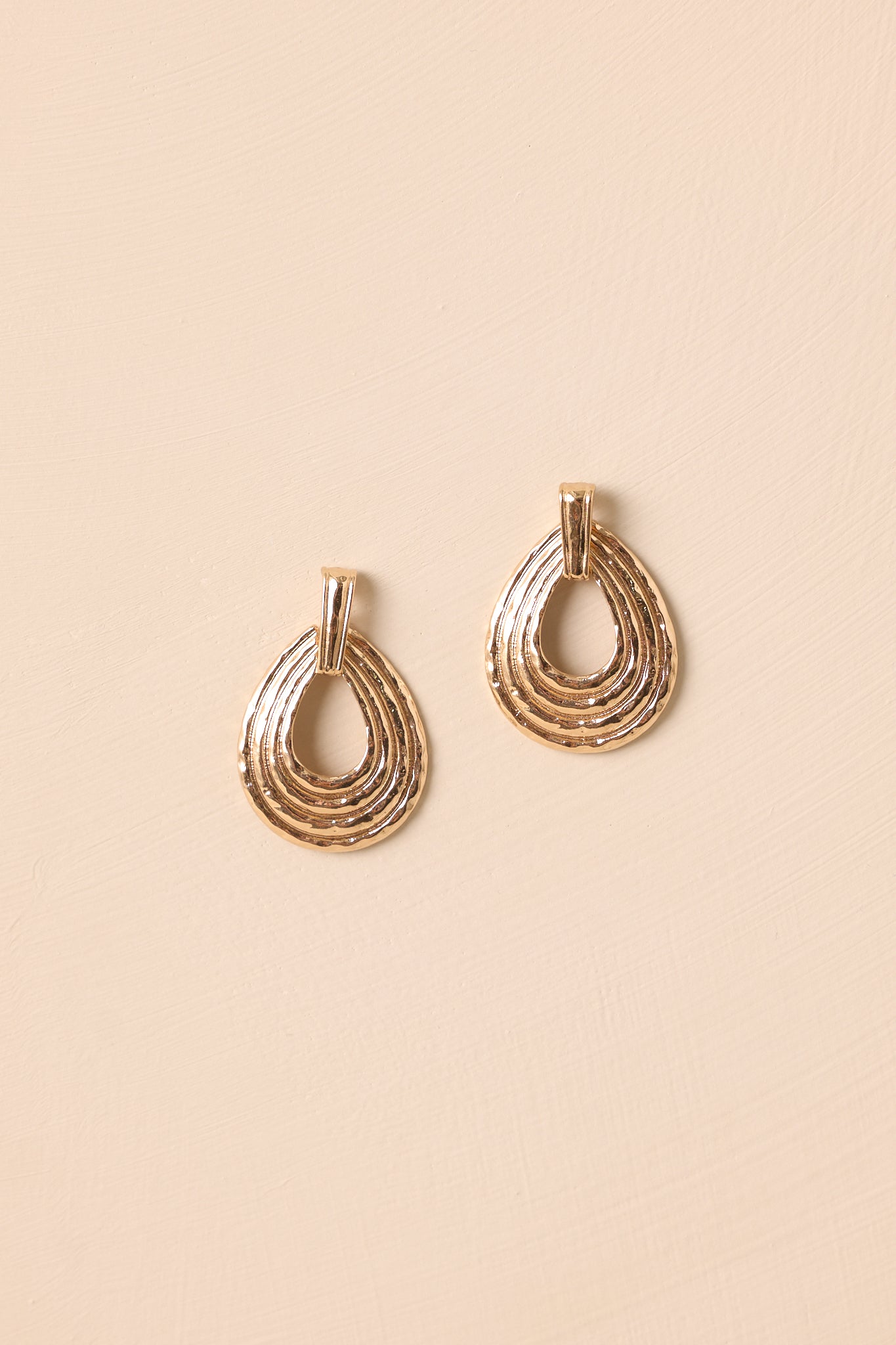 A detailed shot of the gold oval earrings highlighting a ribbed texture, hammered finish, and polished edges.