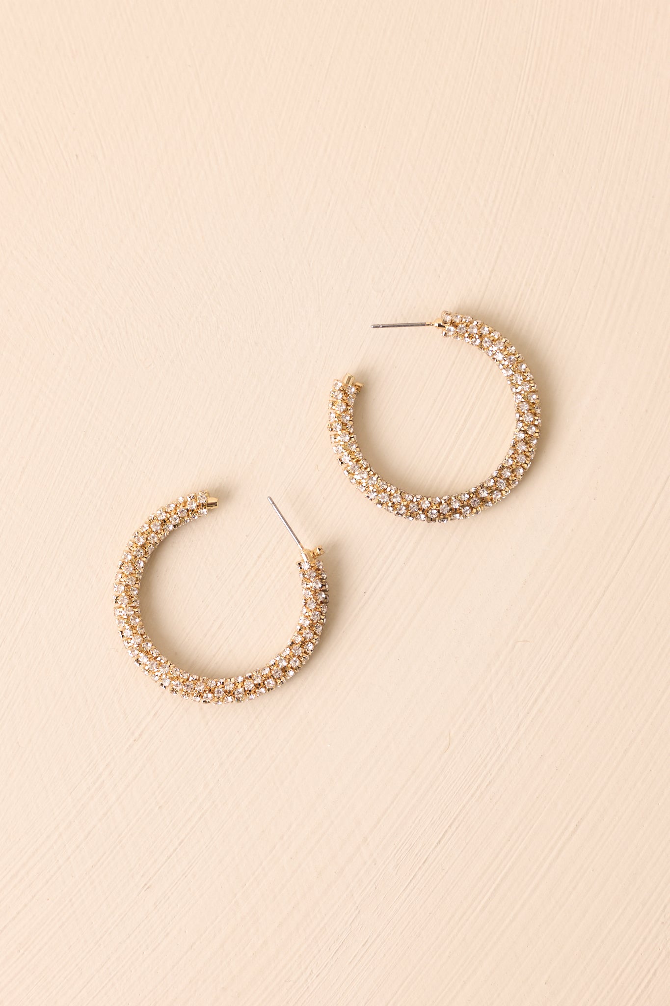 Gold rhinestone pavé hoop earrings displayed on a beige background, showcasing the medium-sized design.