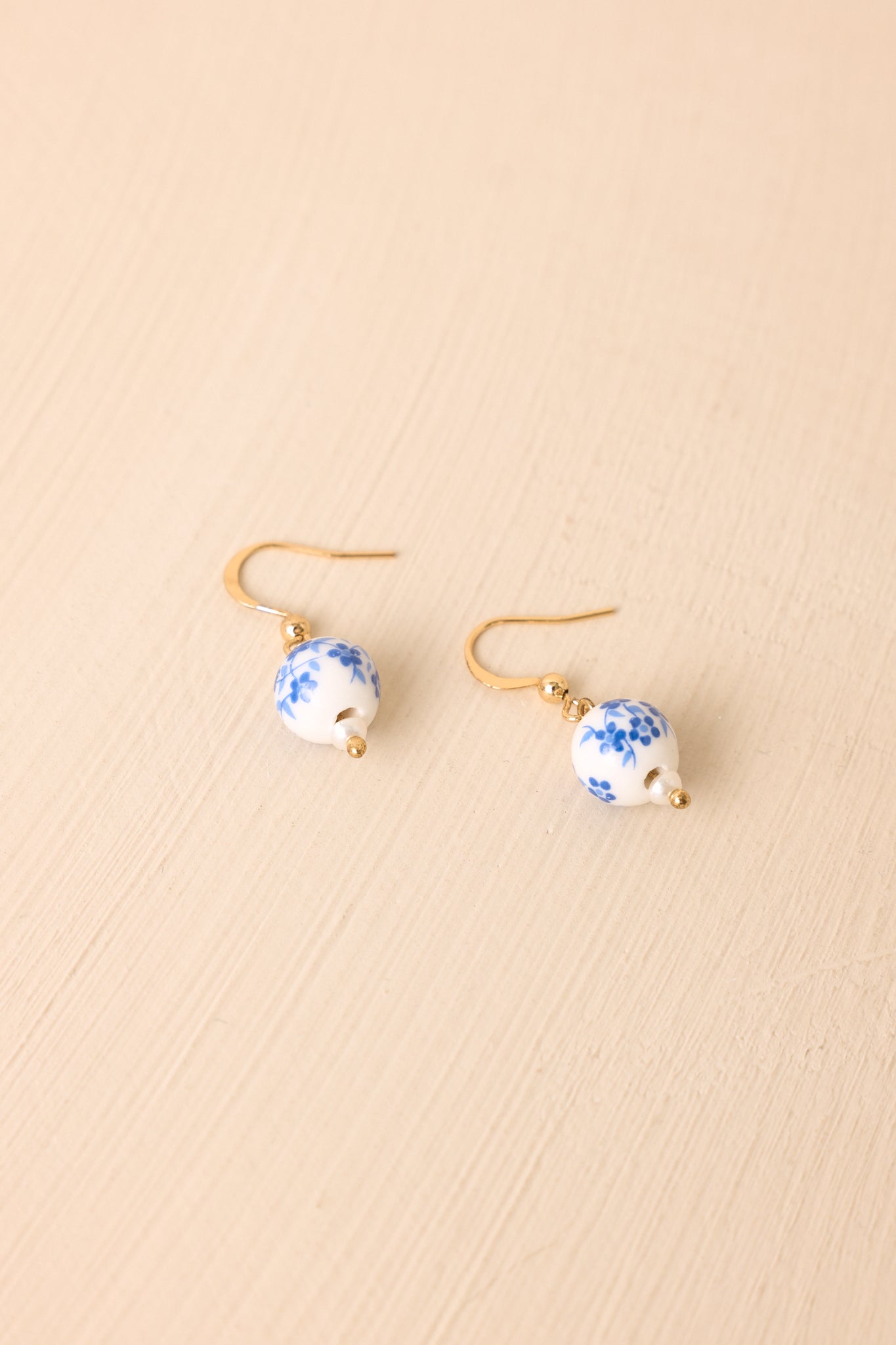 Pair of gold-tone drop earrings with porcelain-style beads photographed against a soft beige background.