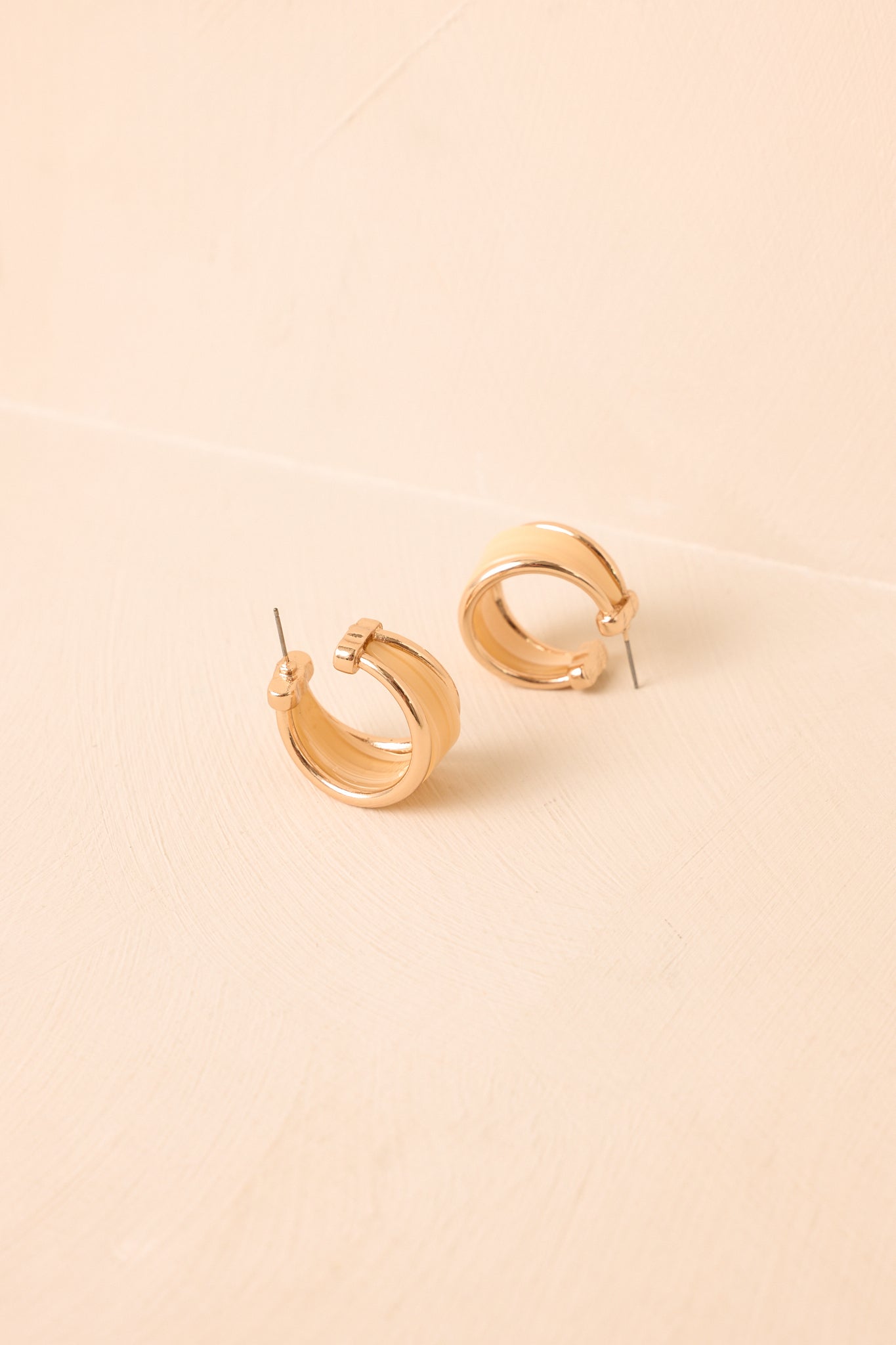 Gold resin hoop earrings displayed against a beige background, highlighting their layered construction and translucent center.