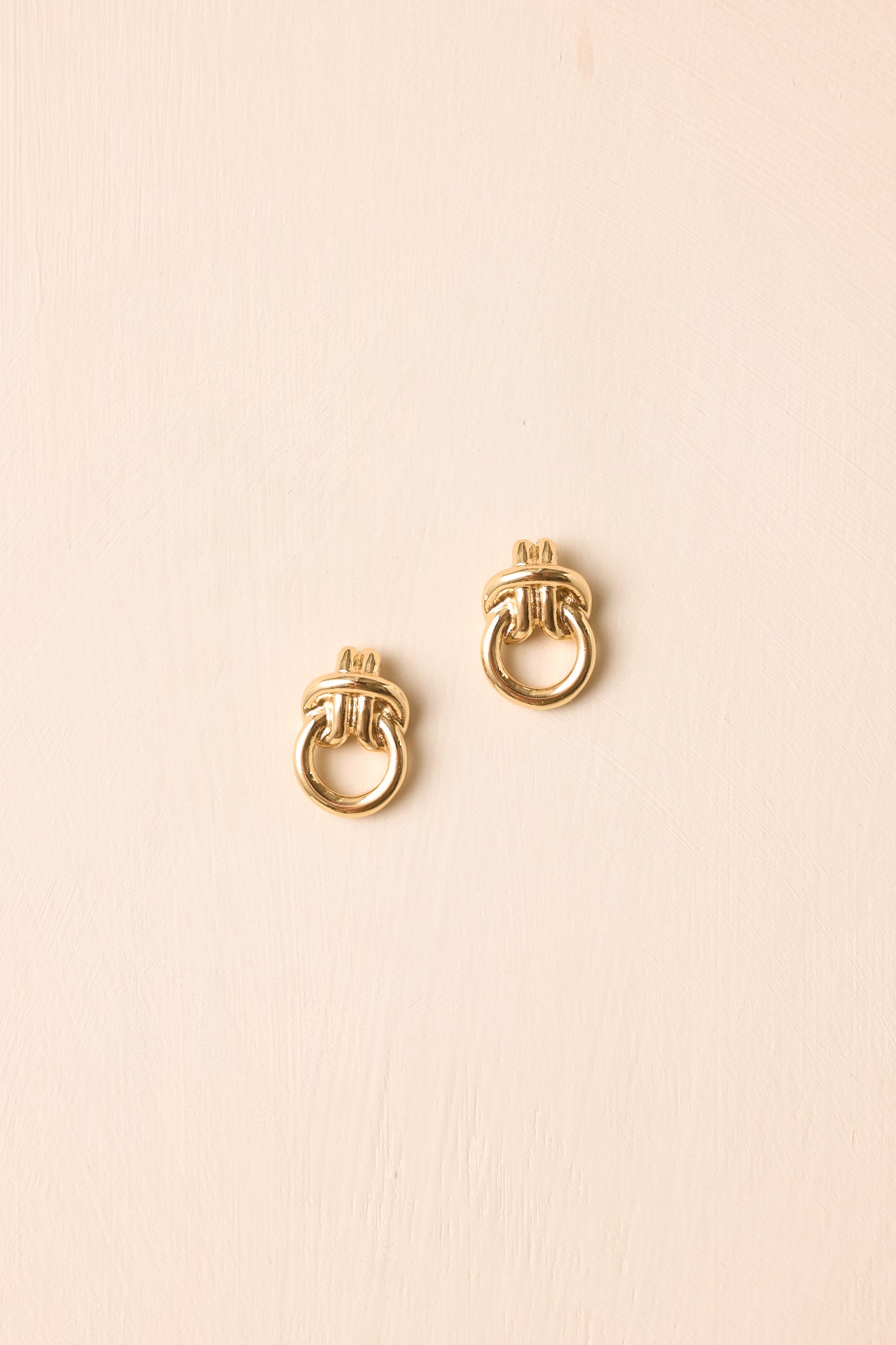 Gold sculptural stud earrings displayed against a beige background, highlighting their smooth curves, polished finish, and lightweight design.