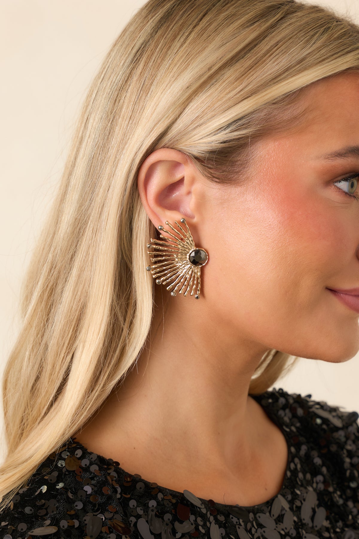 Statement gold earrings featuring a glossy black center stone surrounded by rounded gold spokes.
