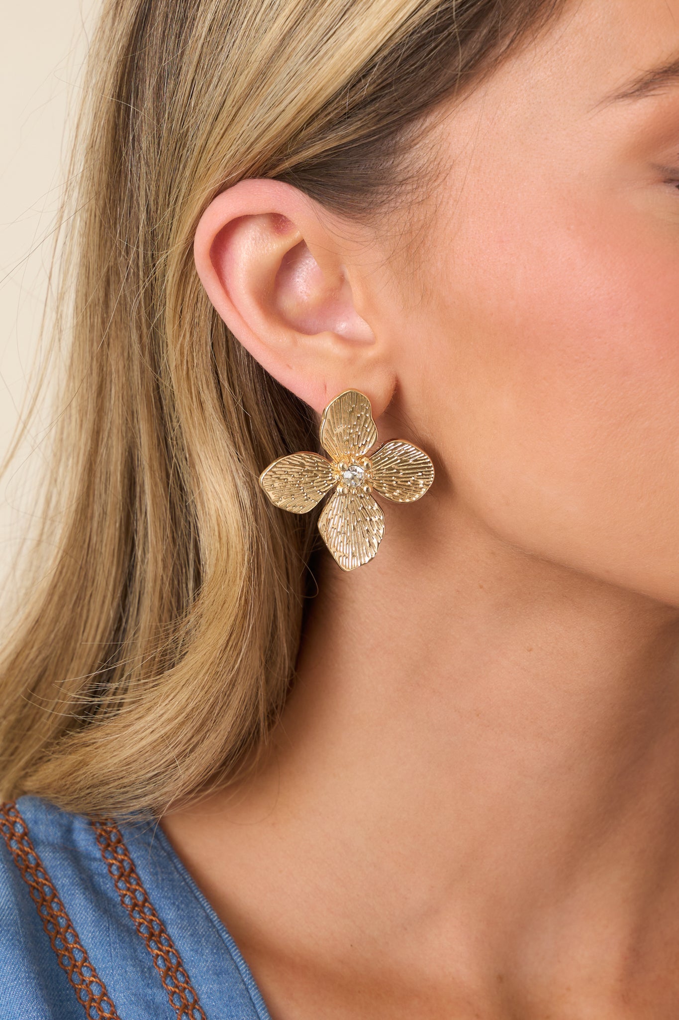 Cropped view of gold statement earrings with sculpted floral petals and textured radiant finish.