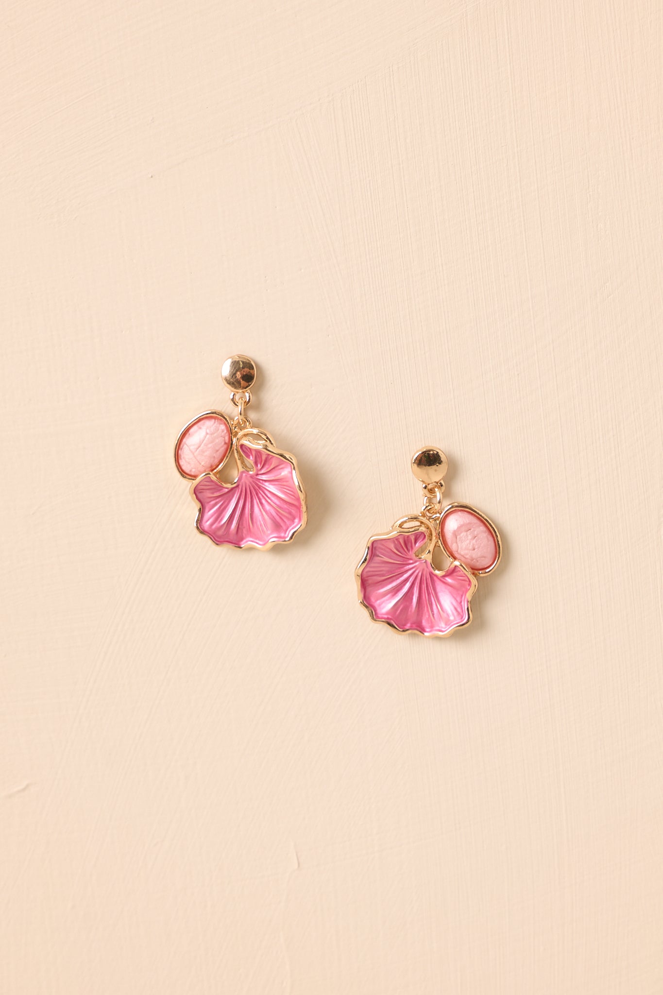 Cropped view of gold stud earrings with pink oval cabochon and floral petal drop.