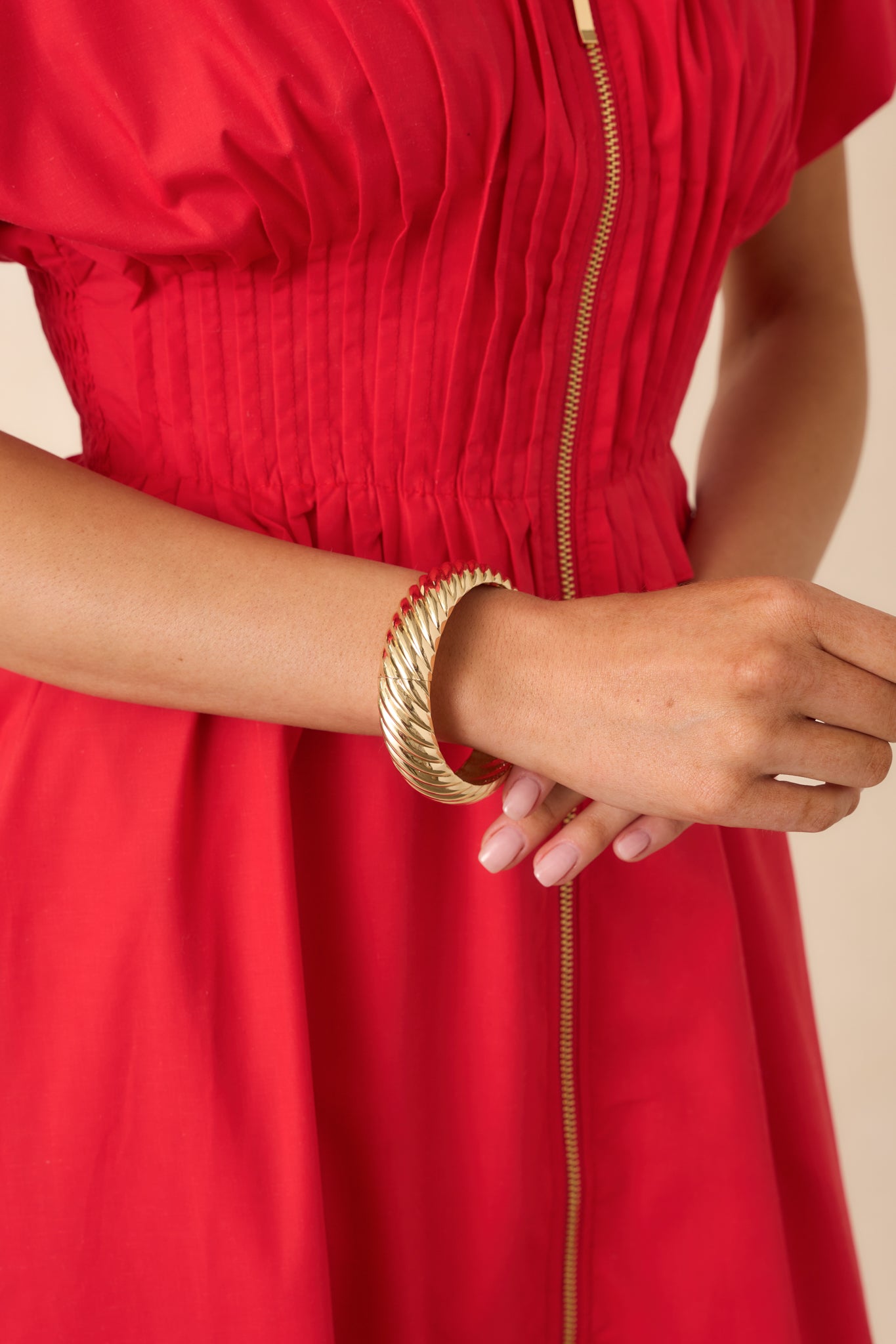Cropped view of the gold-tone bangle showcasing the rigid twisted design and polished high-shine finish.