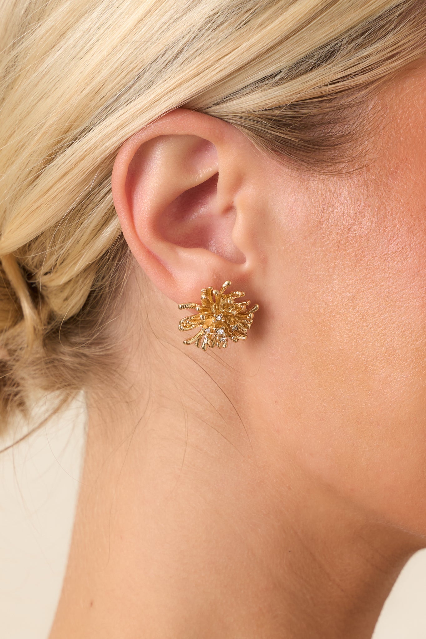 Close-up of the gold-tone earrings featuring freeform curved strands, delicate crystal accents, and a polished sculptural finish.