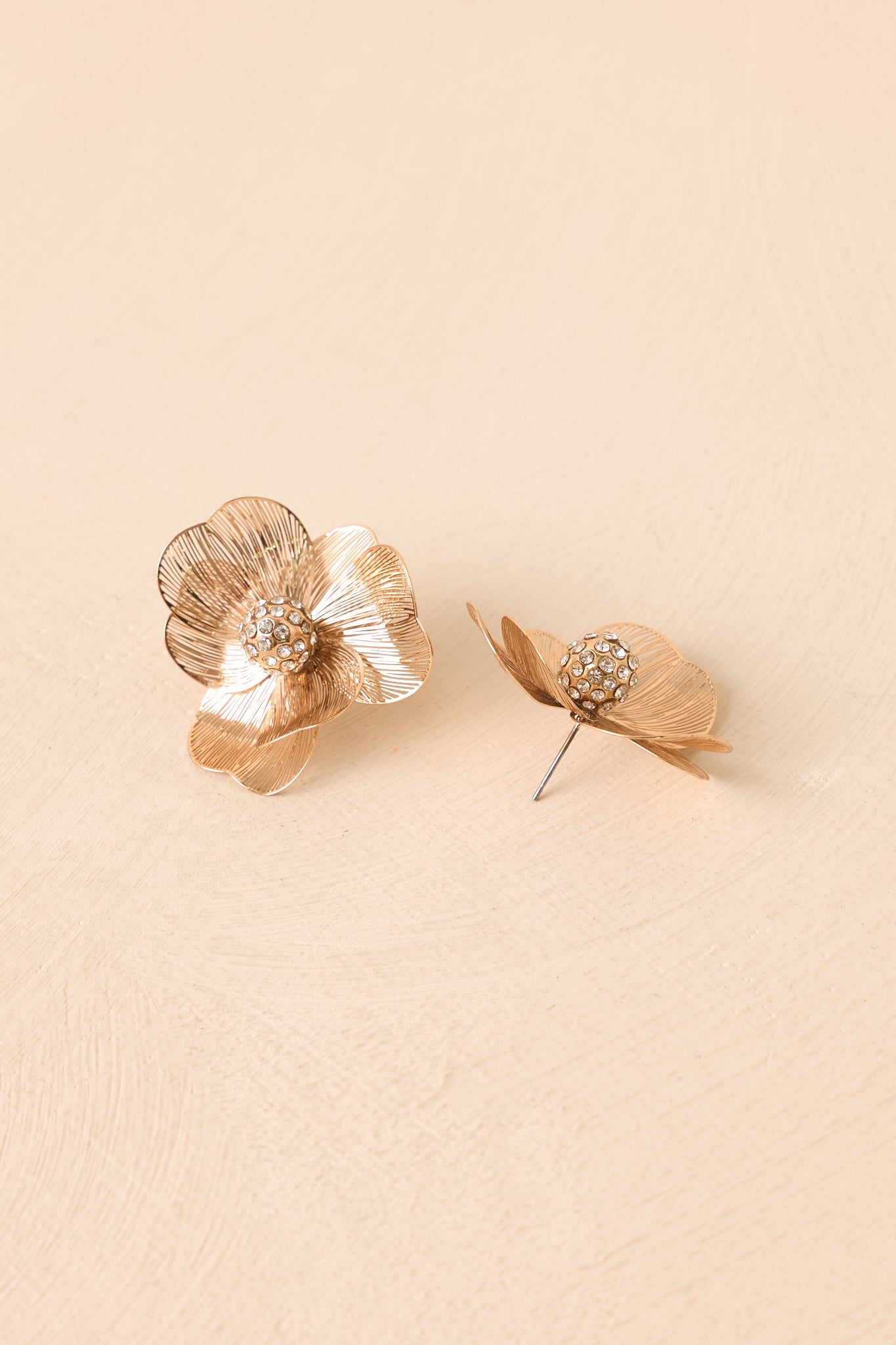 Detailed view of gold-tone flower earrings showcasing dimensional petals and shimmering crystal accents.