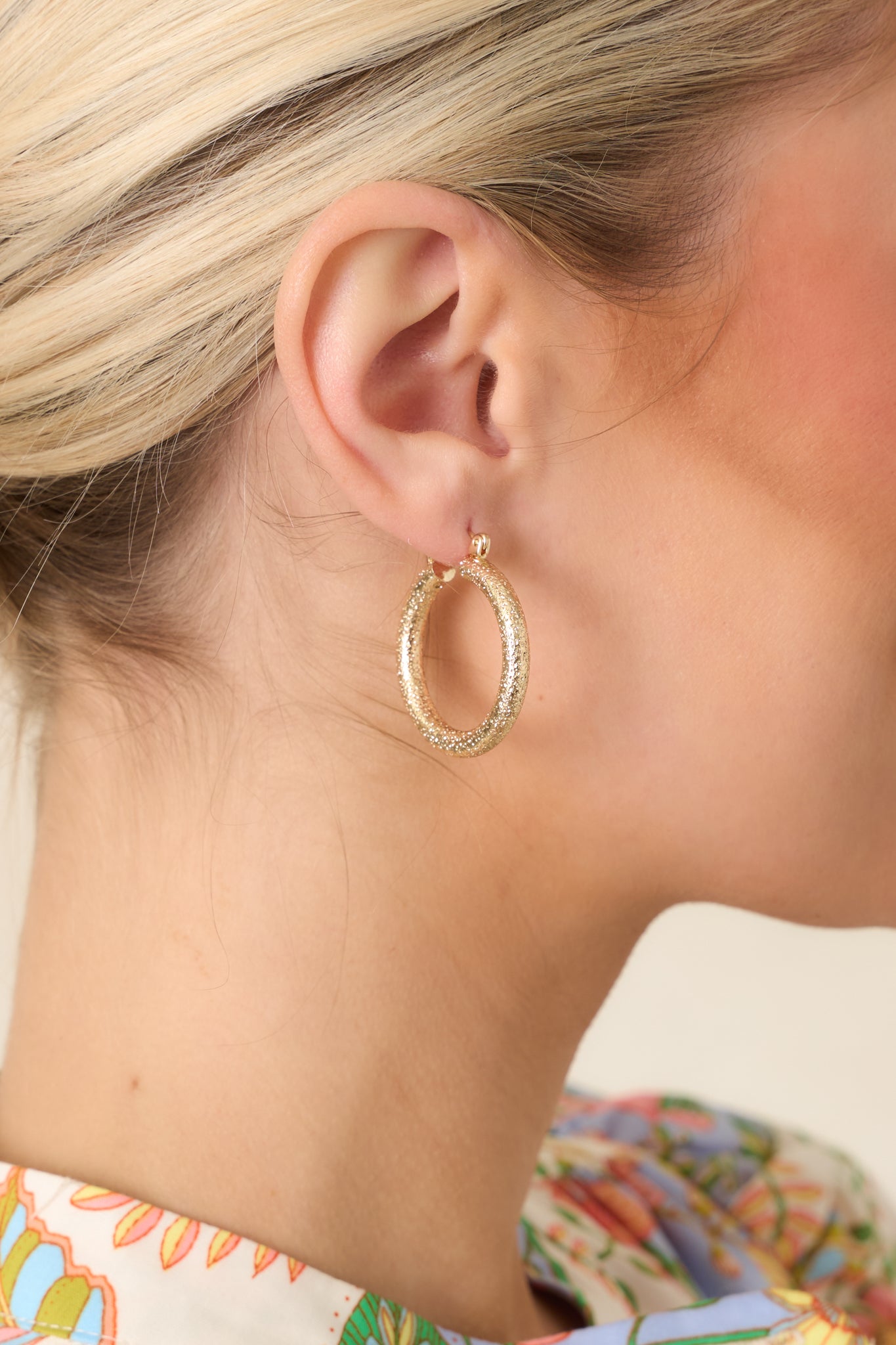 Detailed close-up of gold-tone hoop earrings emphasizing the softly textured surface and dimensional light-reflecting finish.
