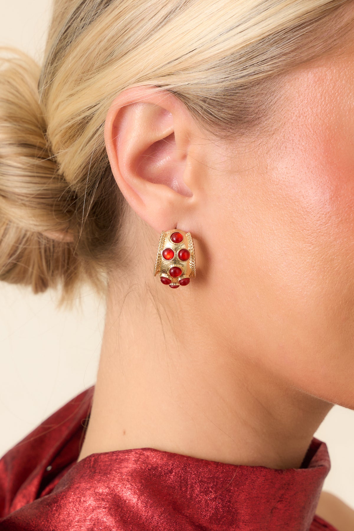 Chunky gold-tone hoop earrings featuring glossy round red stones, curved silhouettes, and textured metallic detailing.