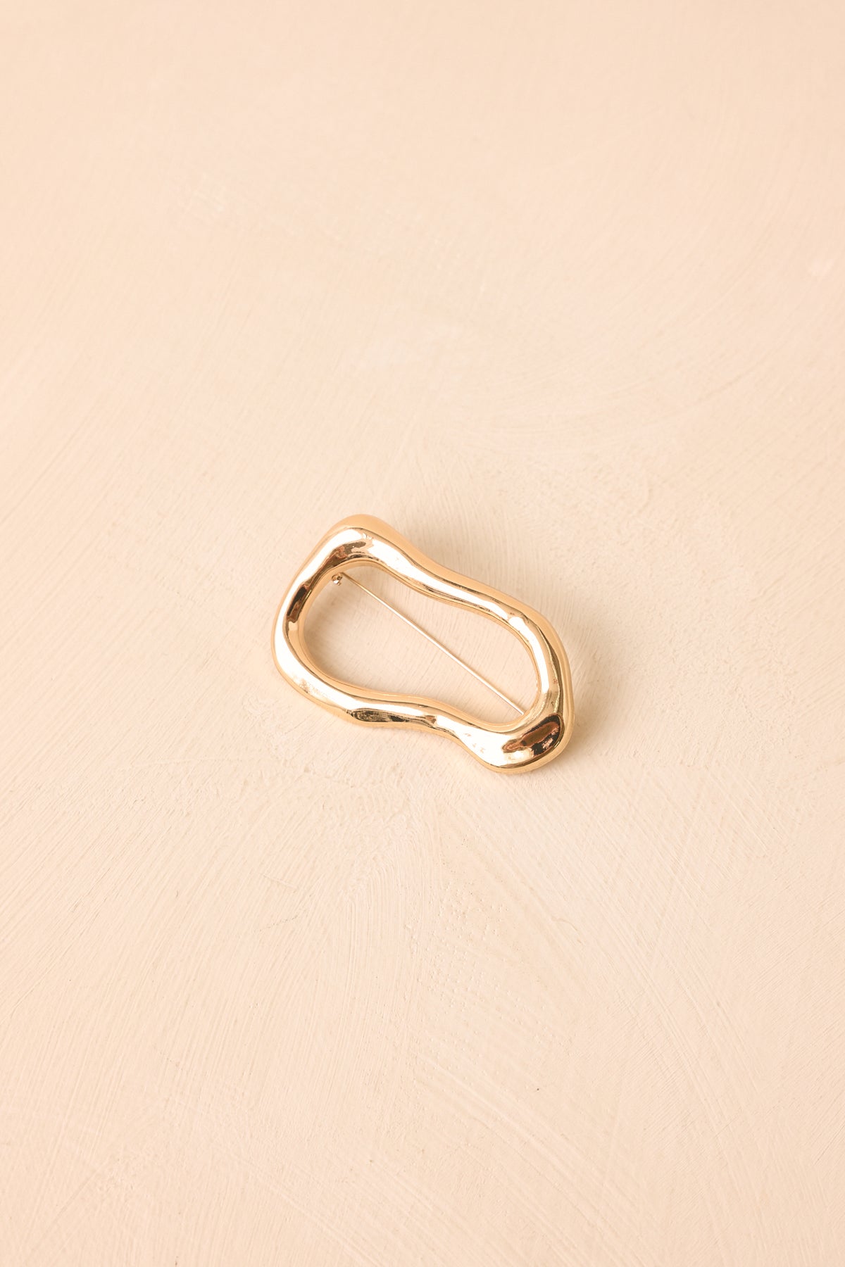 Gold-tone brooch featuring a polished open-frame silhouette with a modern artistic shape and refined metallic finish.