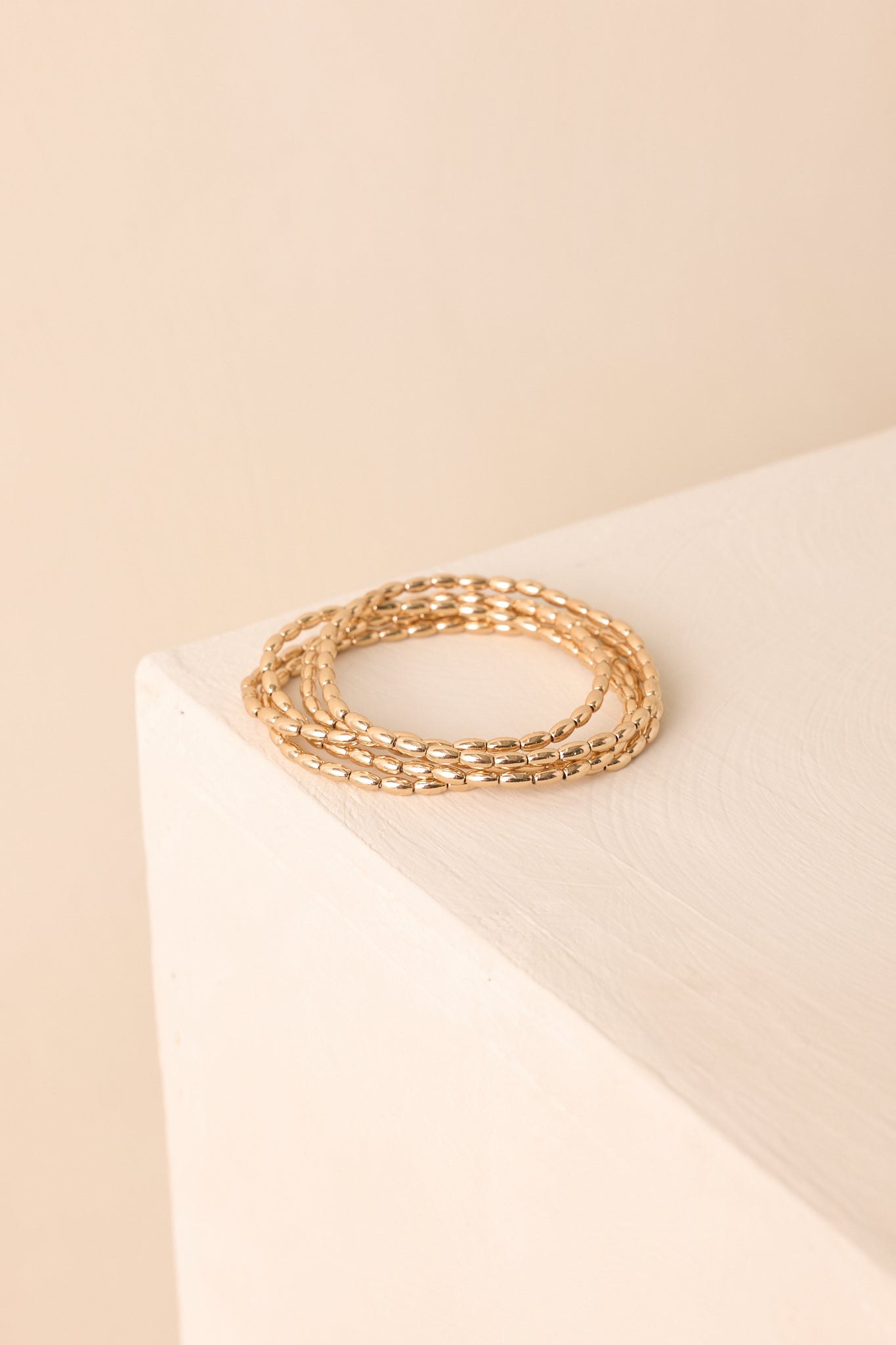 A cropped photo showing a set of five gold stretchy bracelets with elongated oval beads and polished finish.