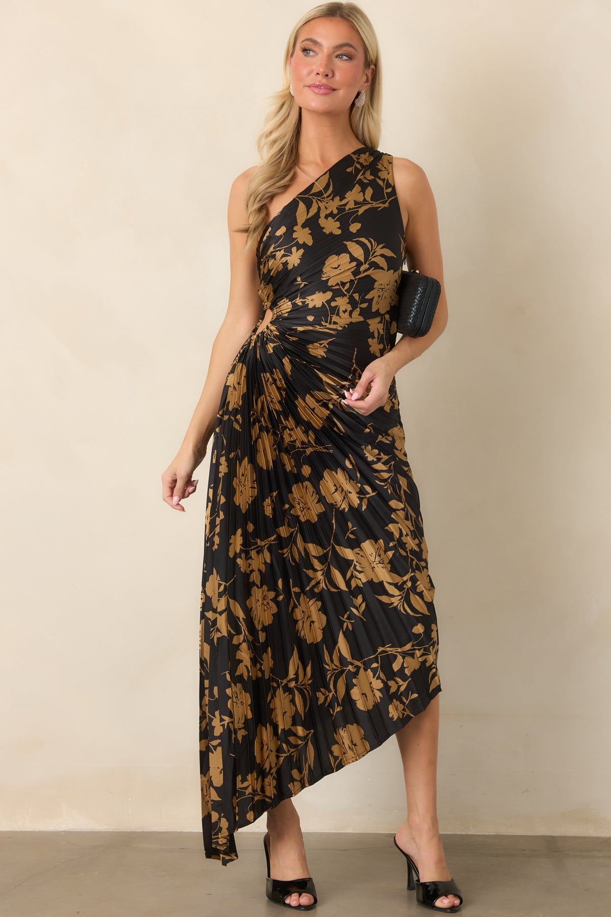 Golden floral detailing contrasts against the sleek black satin, while sculpted pleats shape the one-shoulder silhouette.
