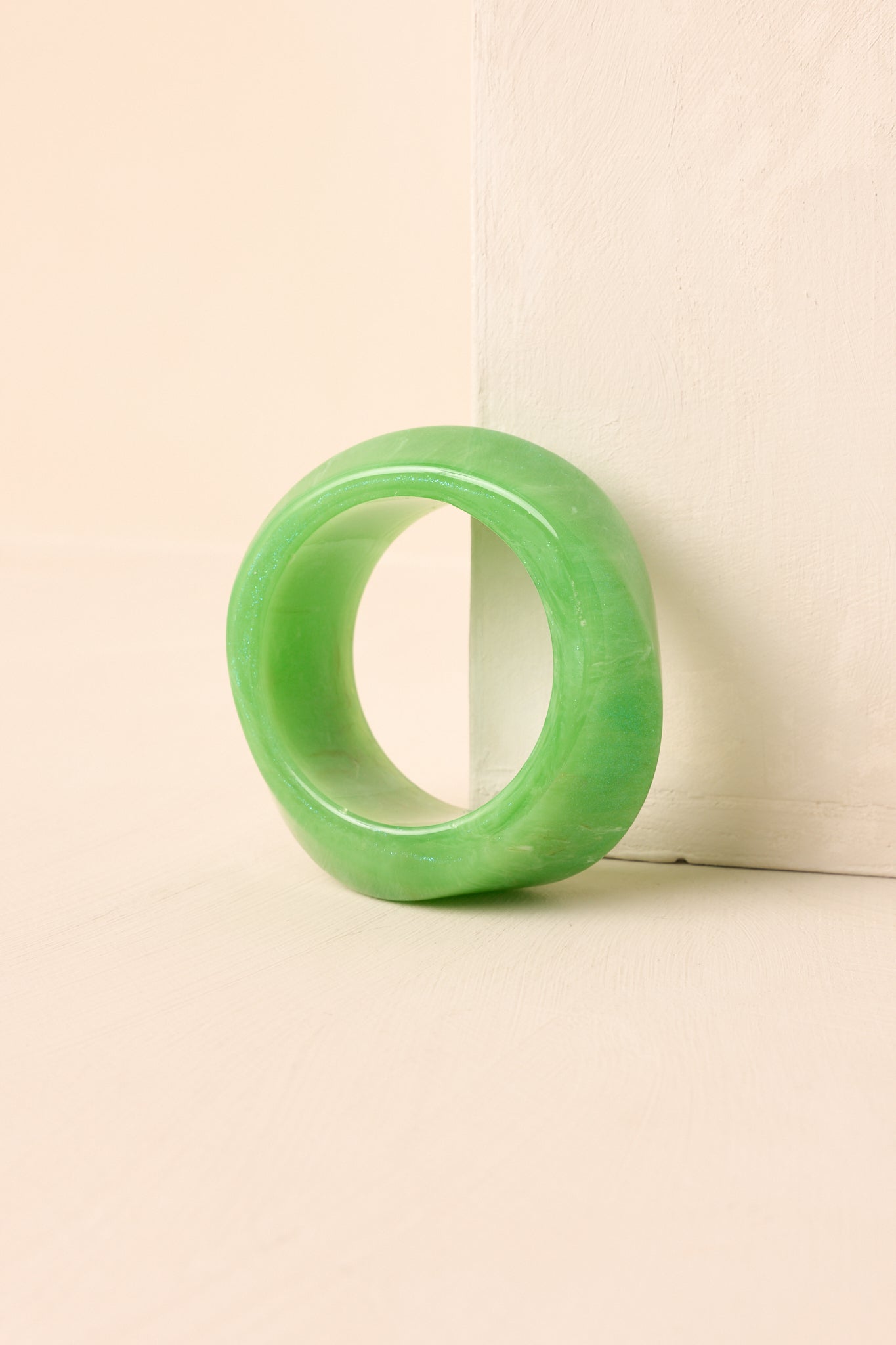 The green acrylic bangle on a beige background, emphasizing its chunky width and shimmering glitter accents.