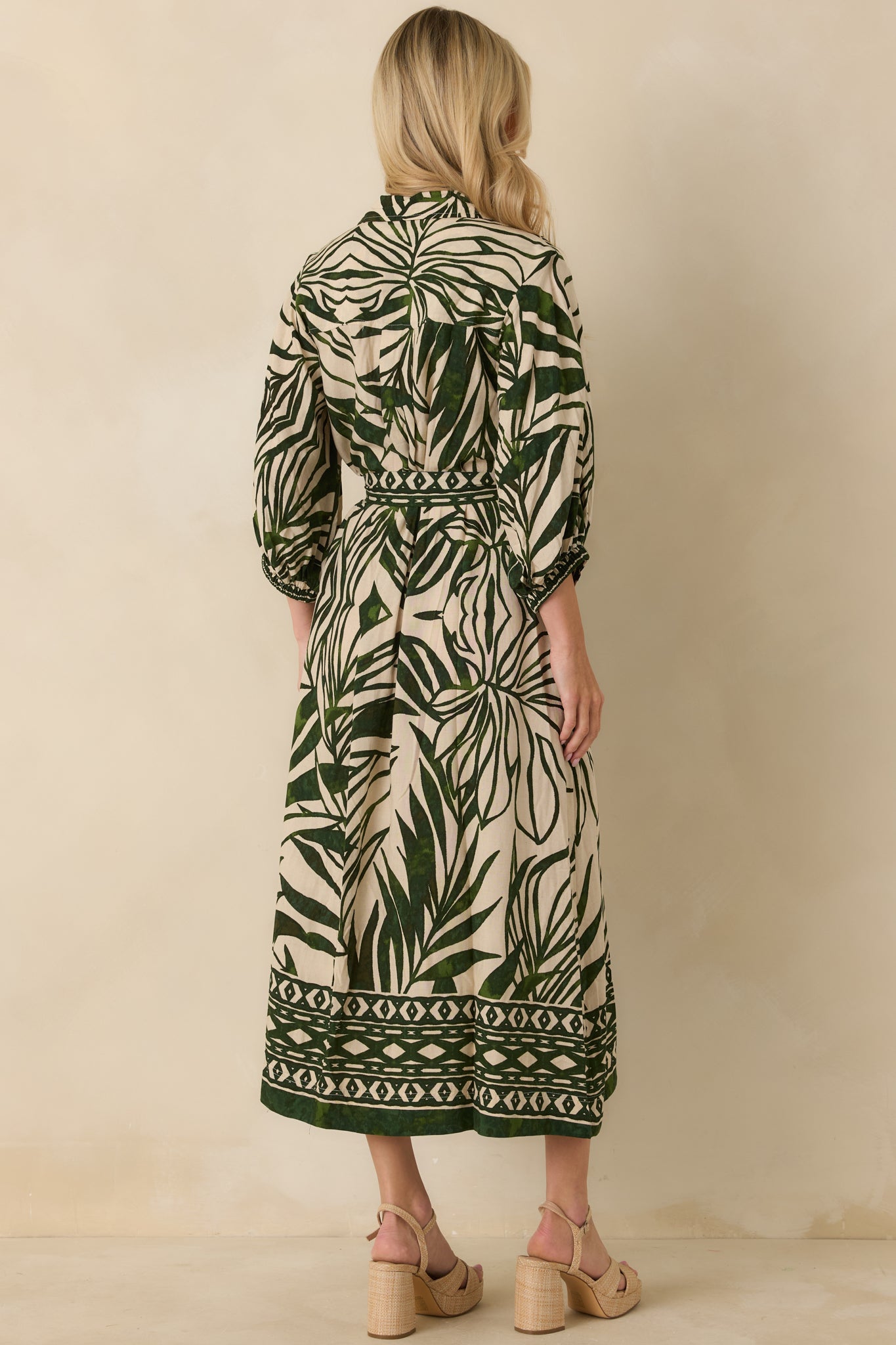 Back view of green and beige tropical print maxi dress featuring box pleat detail and flowing skirt.