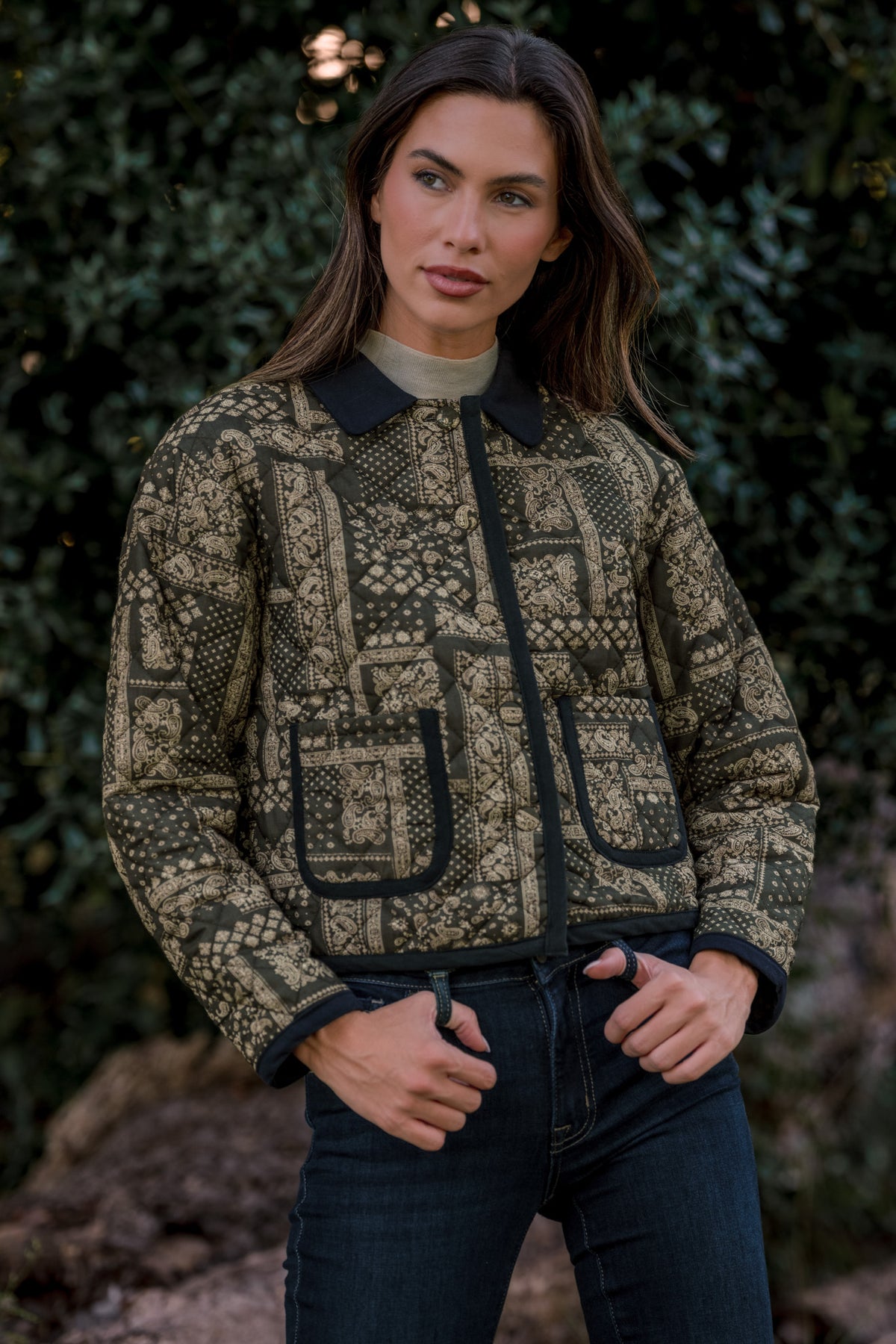 Model wearing an green and ivory patchwork-print jacket with a black collar, black trim, and two front patch pockets, paired with dark jeans.