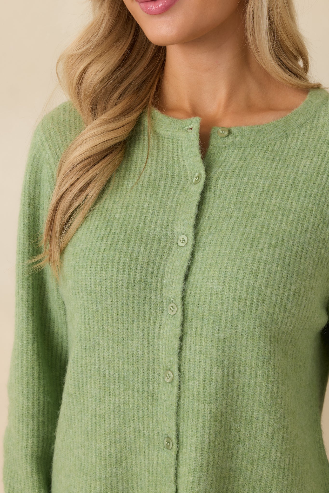 Detailed shot of button closure and ribbed knit texture on green cardigan.