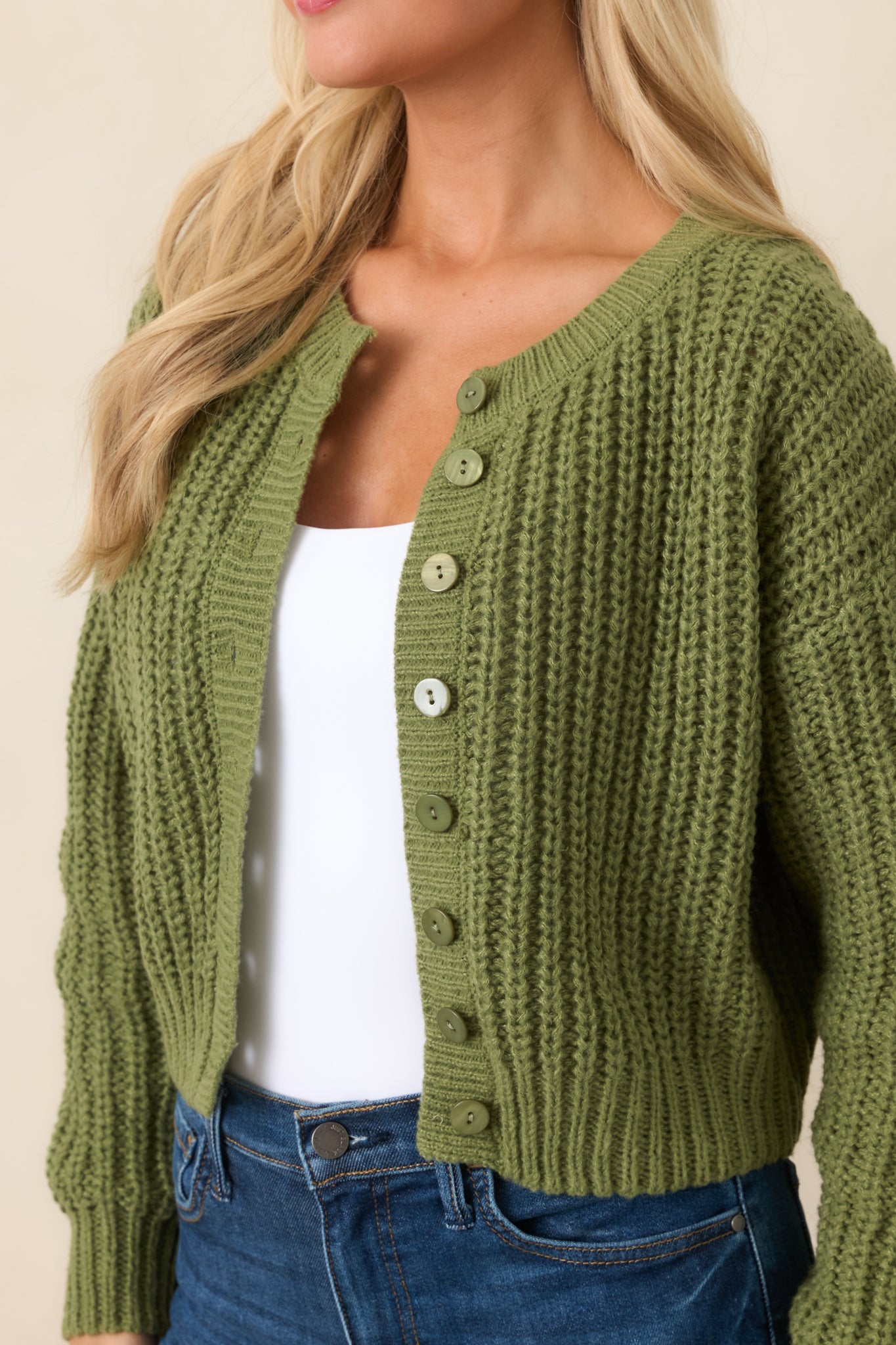 Close-up highlights the chunky cable-inspired knit, tonal marbled button, ribbed trim, and soft green hue.
