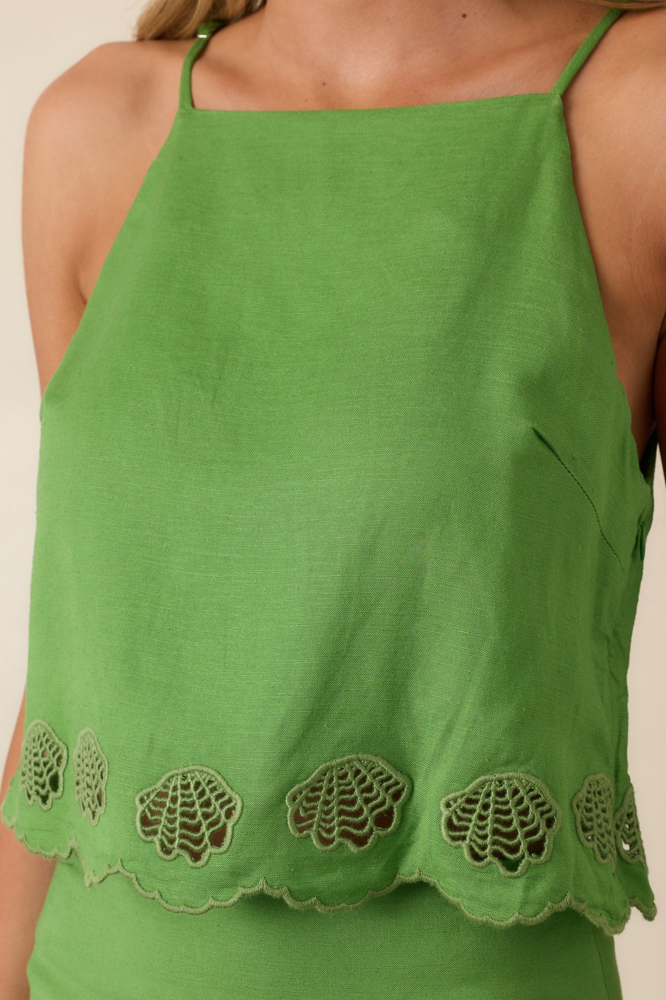 Close-up of the green fabric highlighting scalloped embroidery and shell-inspired cutout detailing on a lightweight woven surface.