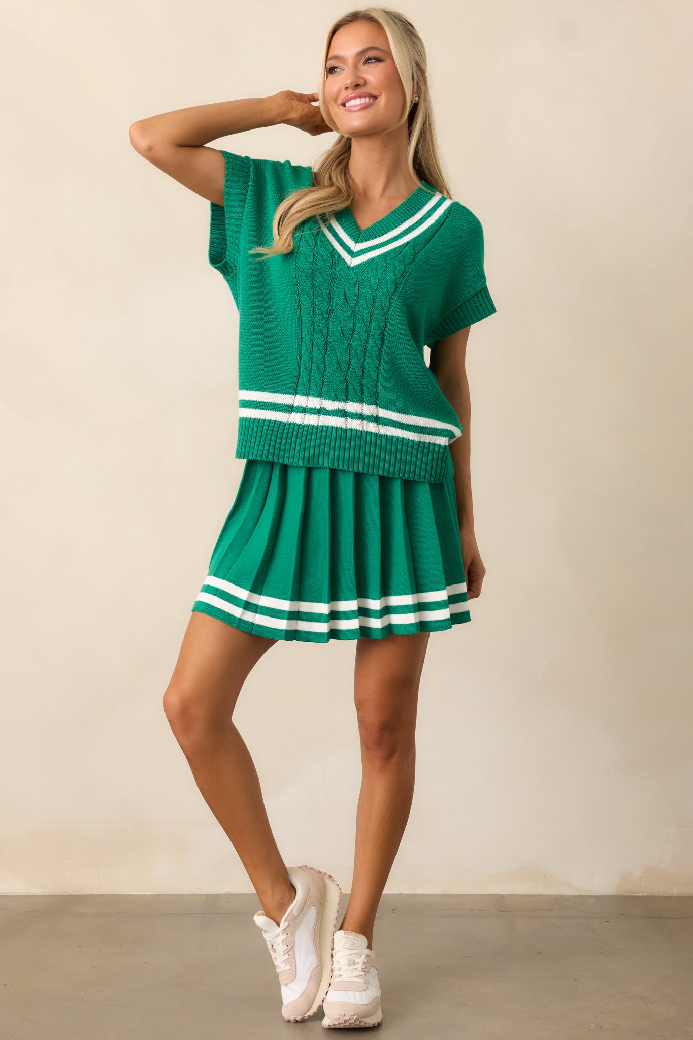Green skirt with a pleated design, elastic waistband, and white stripe detailing along the bottom hem, made from lightweight knit fabric with built-in stretchy shorts.