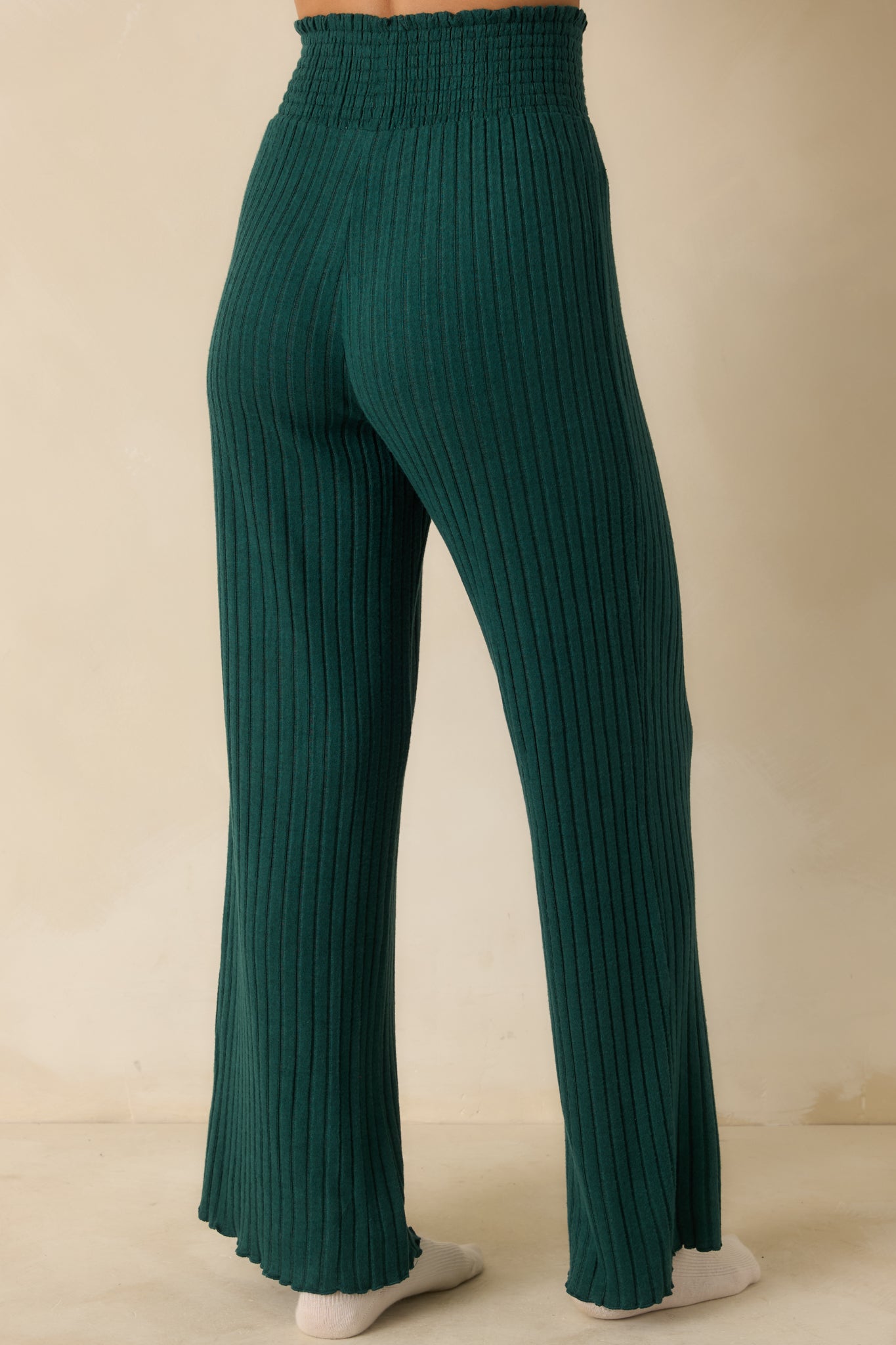 Back view of green ribbed pants, showing fit-and-flare silhouette, high-rise smocked waistband, and smooth knitted finish.