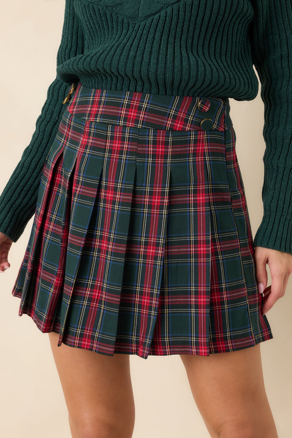 Close-up of the green tartan plaid skirt showing the paired waistband buttons and neatly pressed pleats.