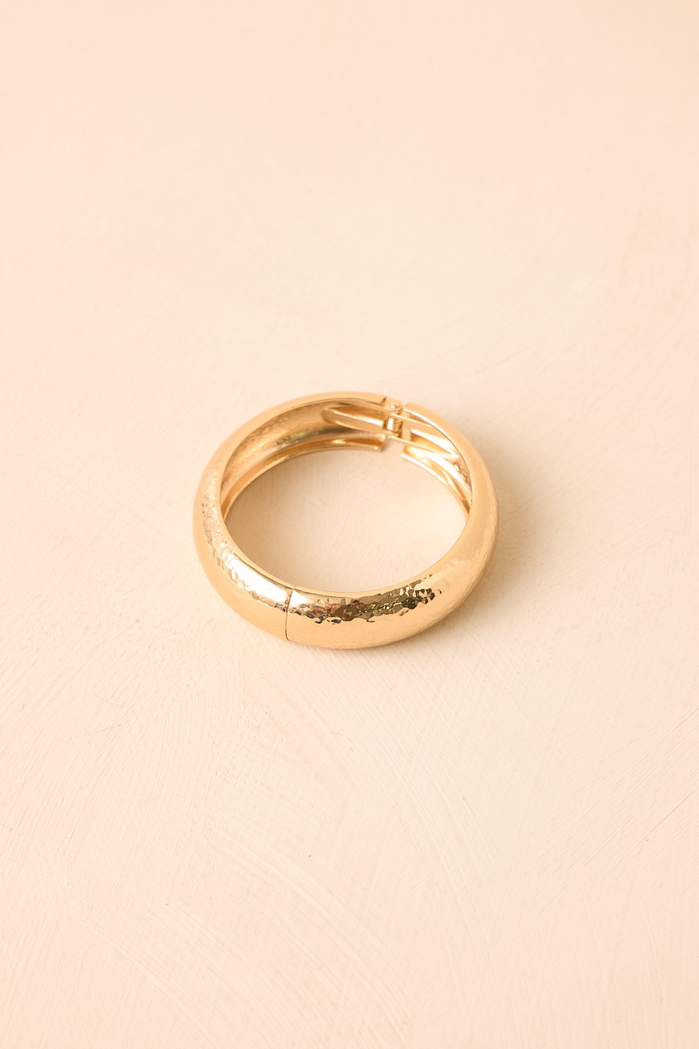 Hammered gold cuff bracelet displayed against a beige background, highlighting its dimensional texture and curved shape.