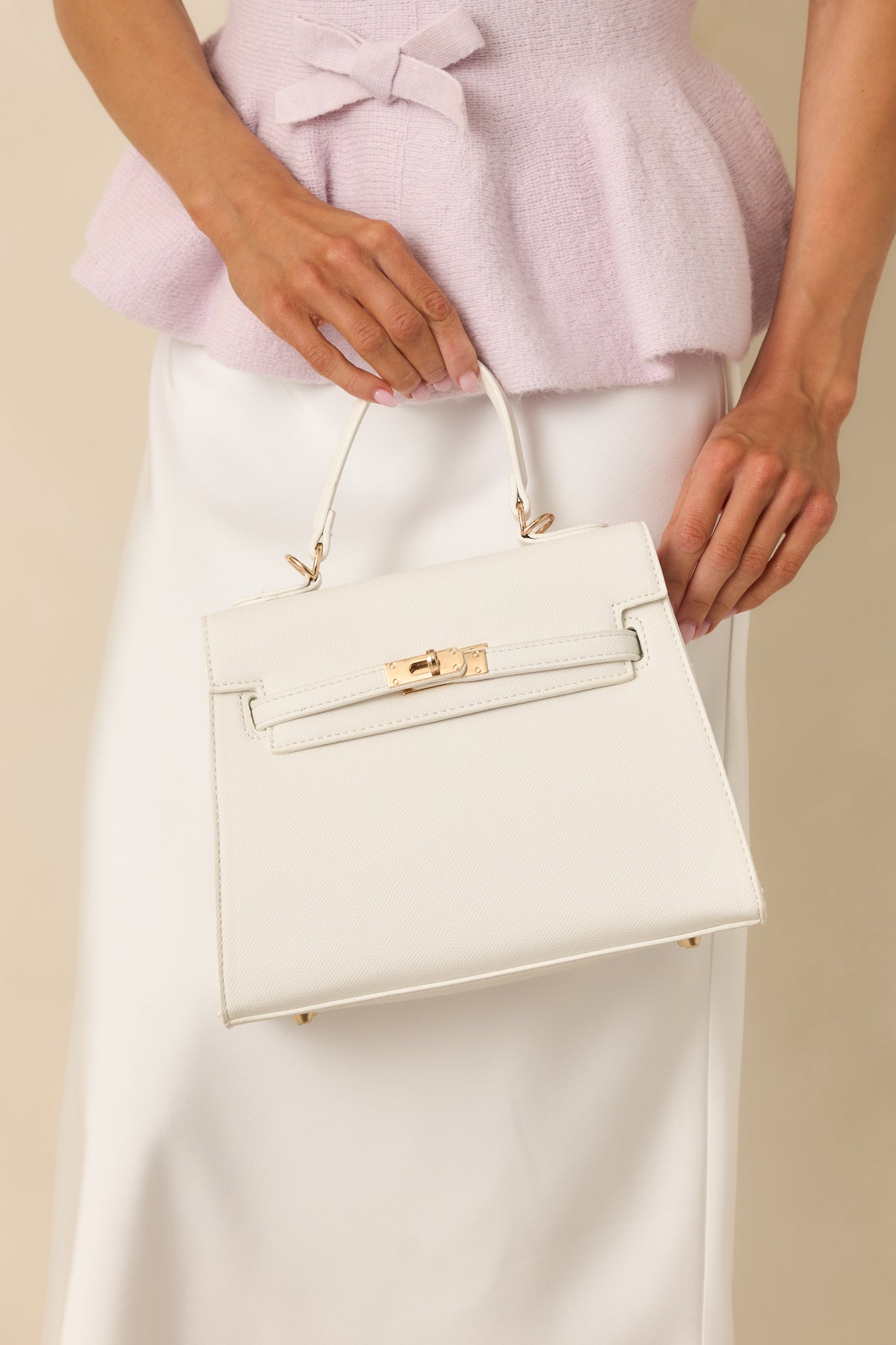 Front view of handbag featuring a top flap secured with two overlapping straps and a twist lock closure.