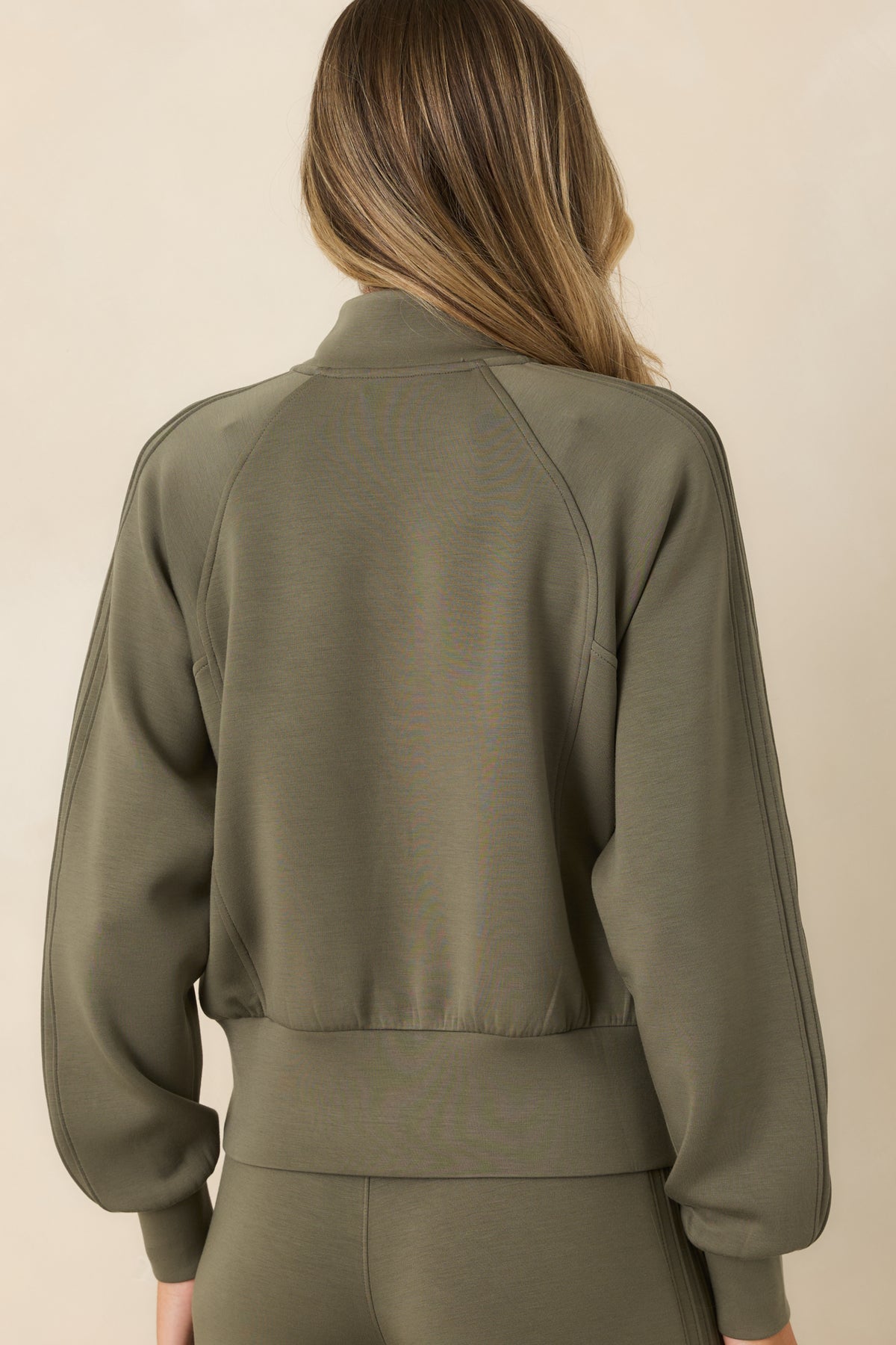 Rear view of the herb green jacket featuring raglan sleeves, fitted cuffs, a wide banded hem, and a clean back silhouette.