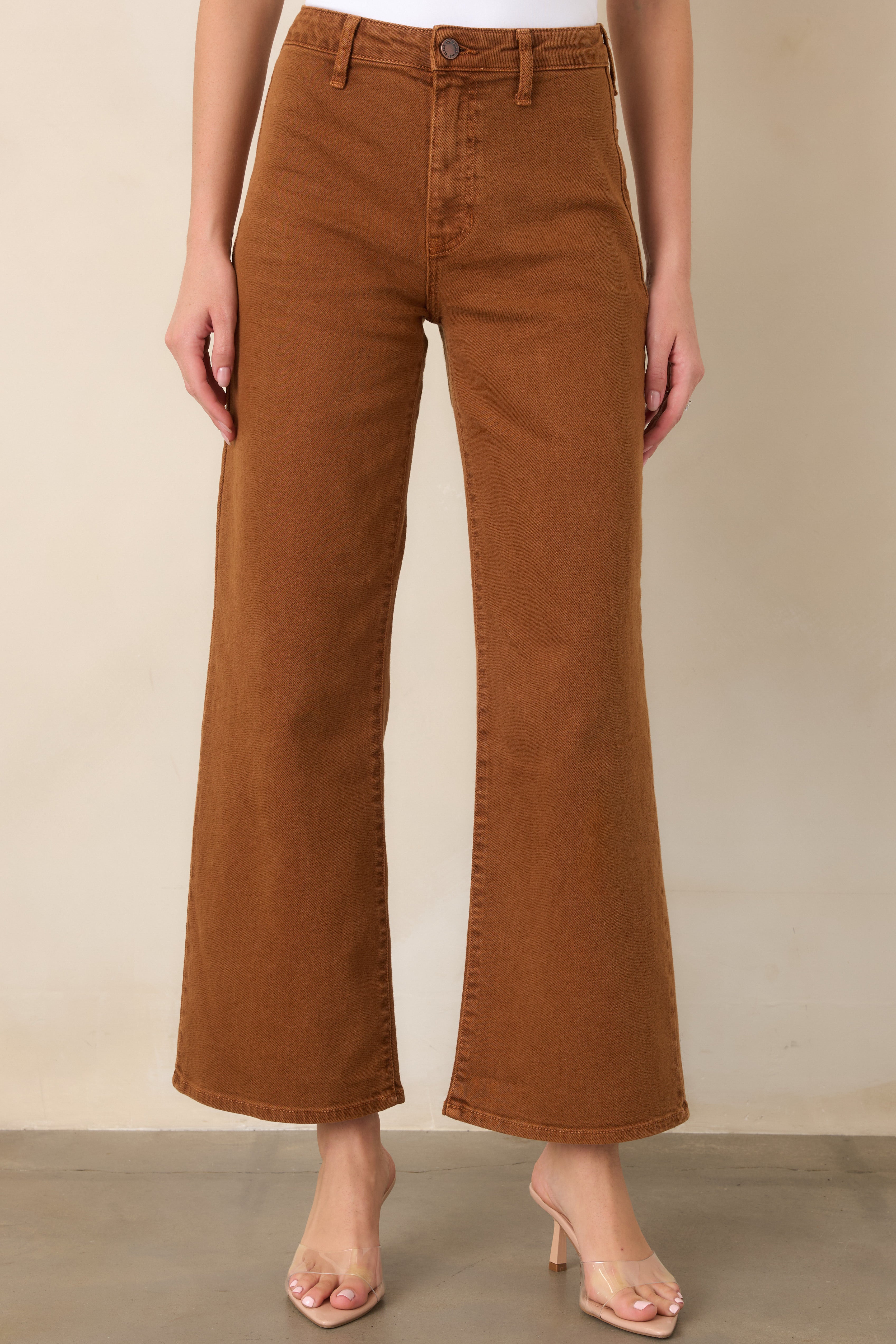 Close view of the high-rise waistband, belt loops, button-and-zip closure, and classic five-pocket design on stretch denim pants.