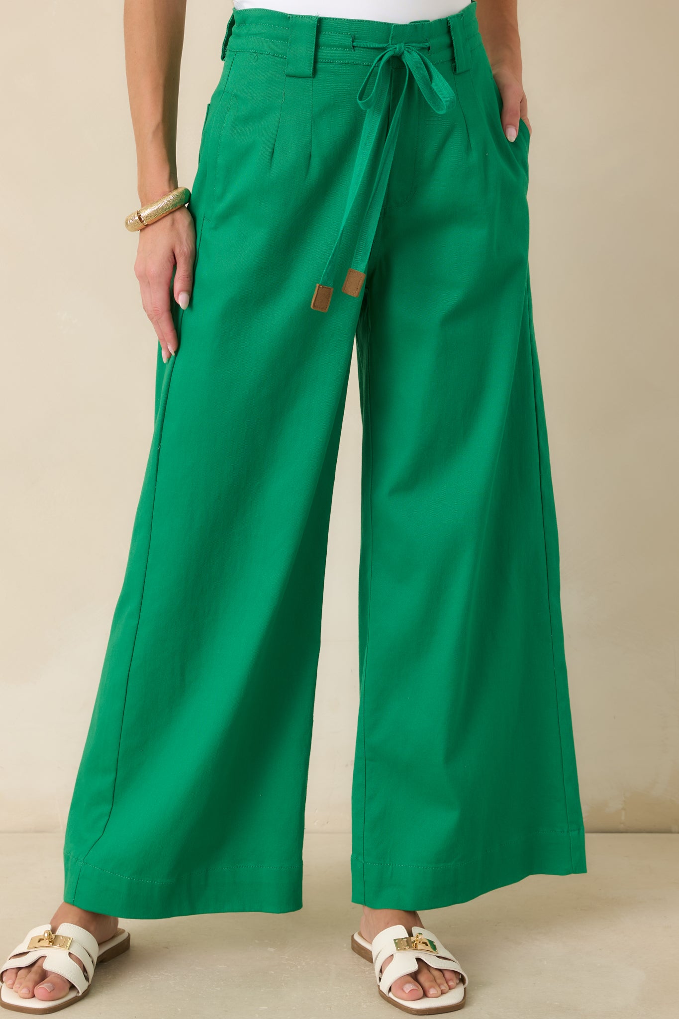 High-rise green pants featuring tailored belt loops, smooth cotton fabric, and refined pleated detailing.