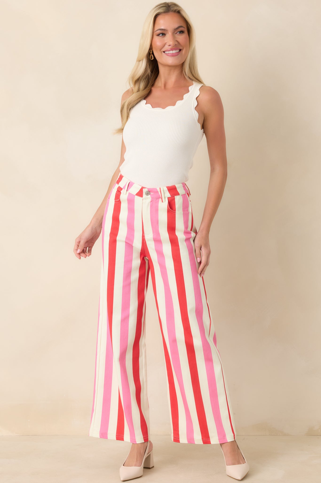 High-rise striped pants in white, red, and pink with zipper and button closure and flowing legs.