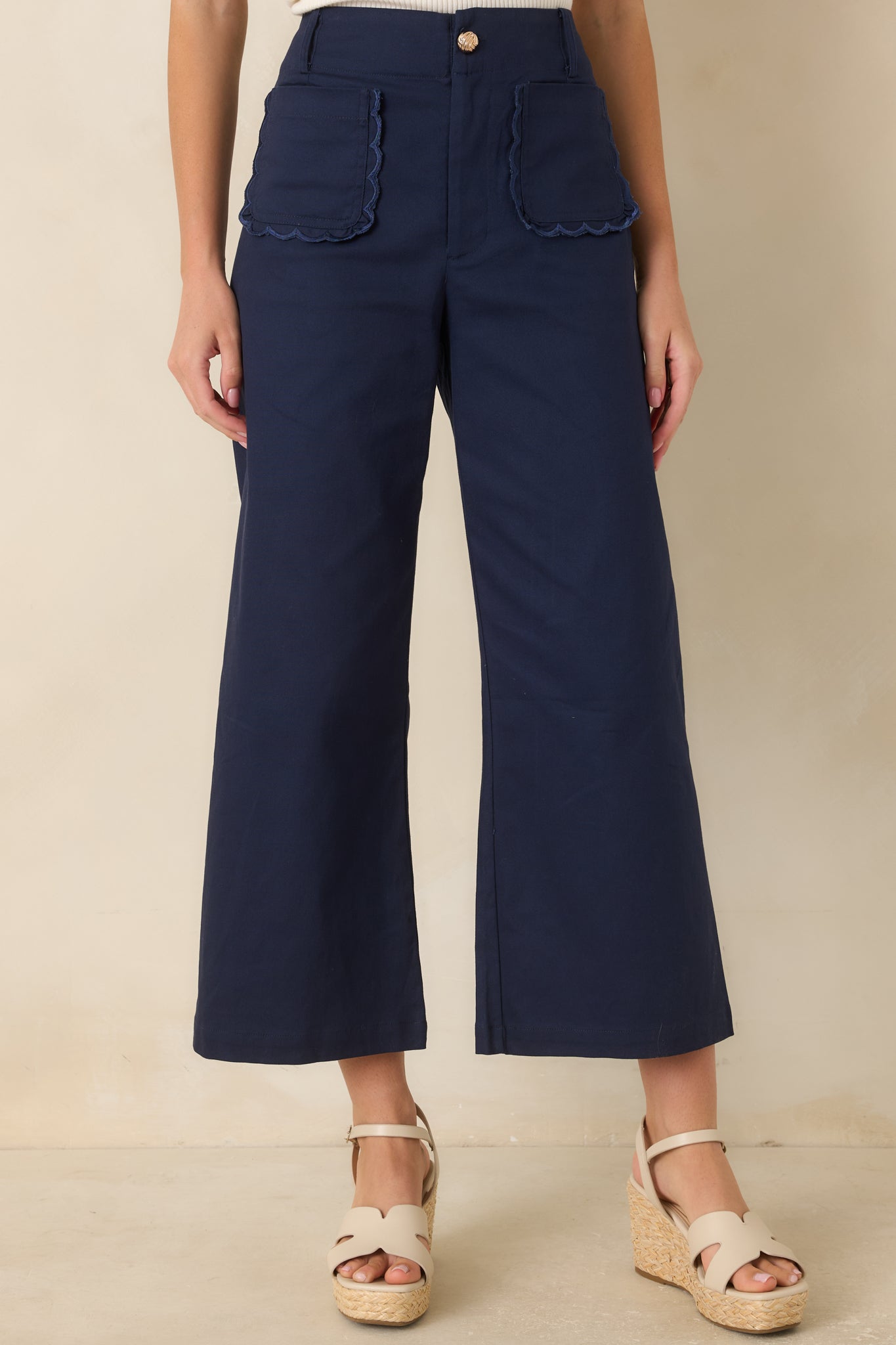 High-waisted cotton blend pants featuring a wide-leg silhouette, cropped ankle length, scalloped patch pockets, and a gold-tone button closure.
