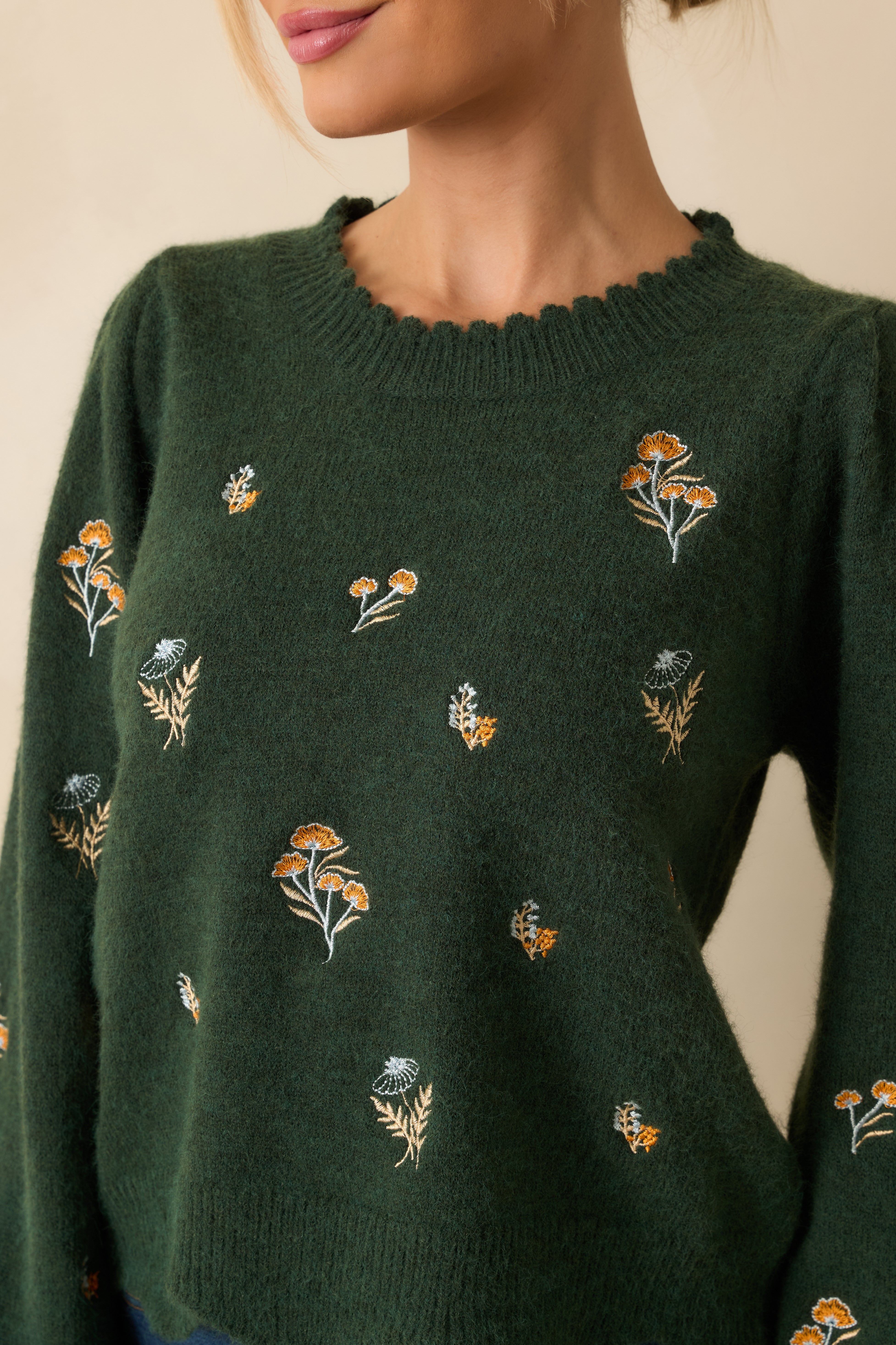 Close-up of the embroidered floral detailing and scalloped crew neckline on the hunter green knit.