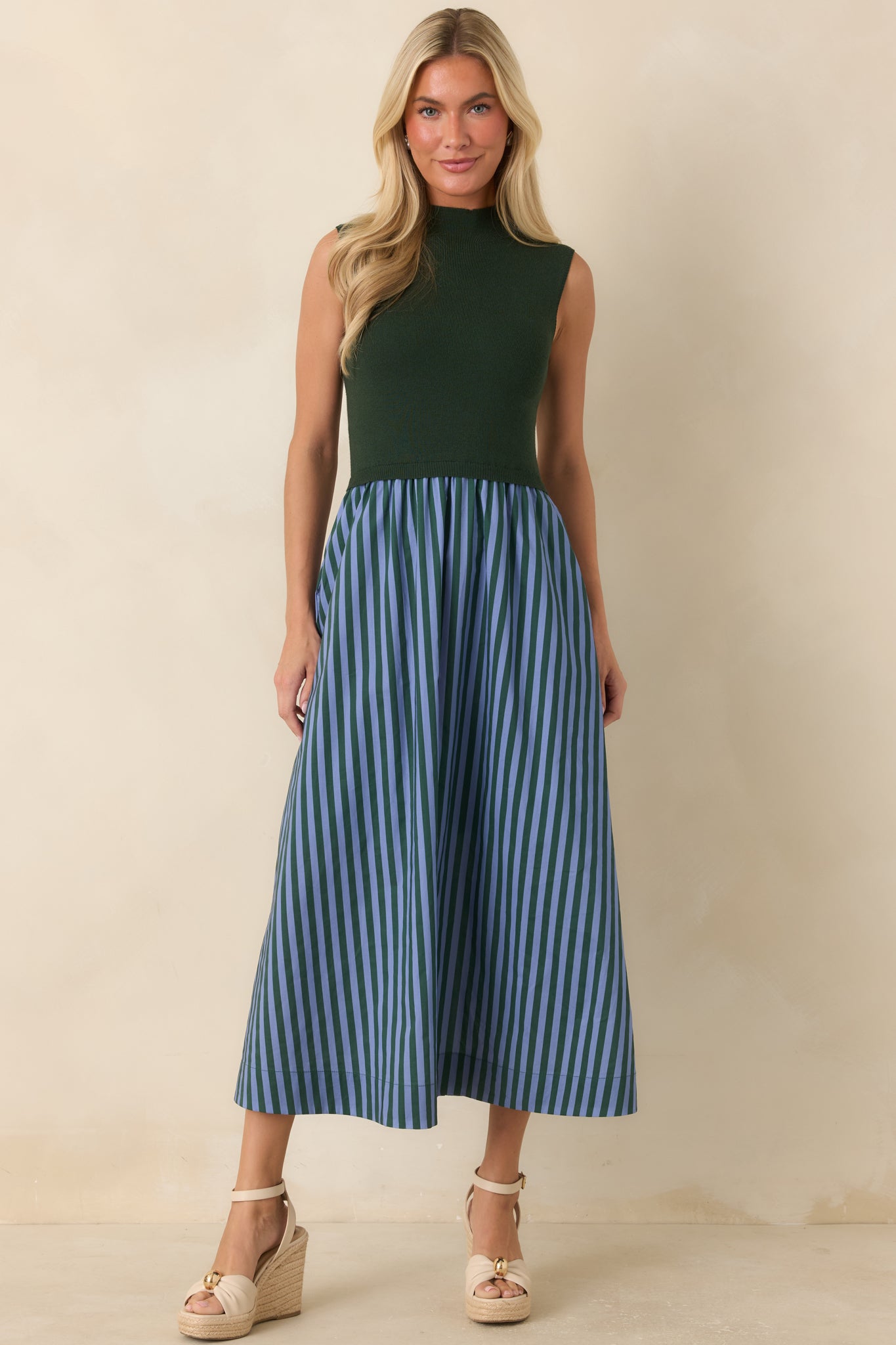 Hunter green knit midi dress showcasing a flattering waistline, soft movement, and light blue striped skirt detailing.