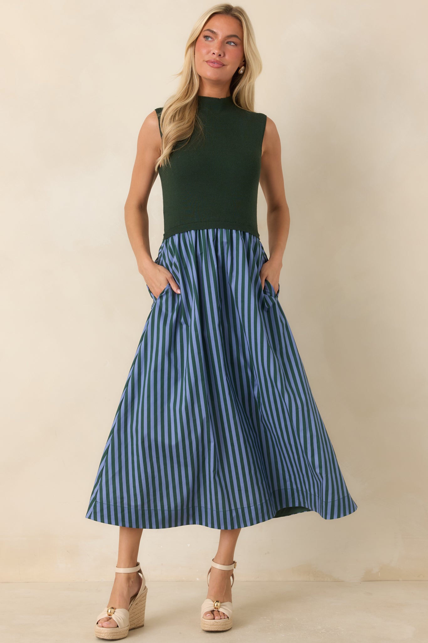 Hunter green midi dress featuring a sleeveless silhouette, refined mock neckline, fitted bodice, and light blue striped A-line skirt