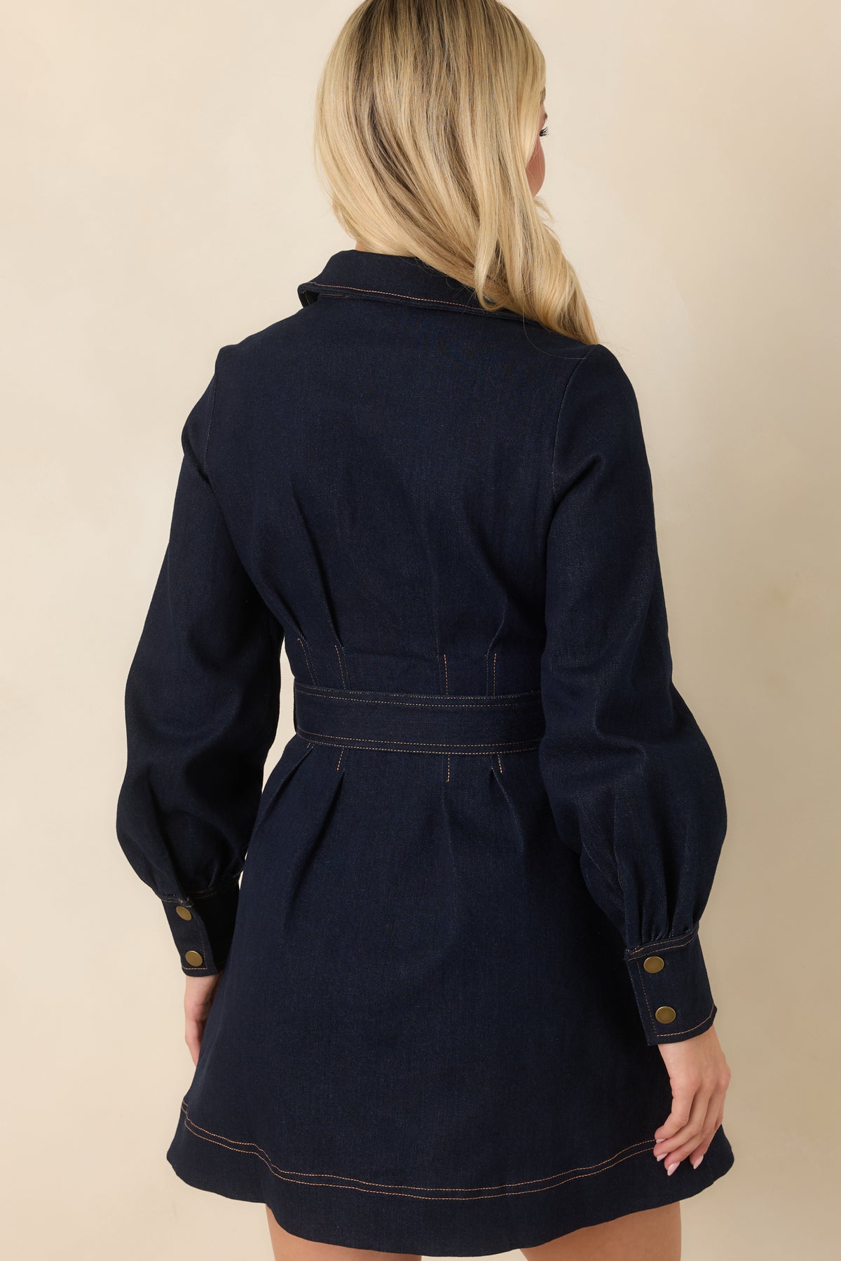 Rich indigo denim mini dress showcasing the long sleeves, defined waist, and gently flared skirt from the rear.