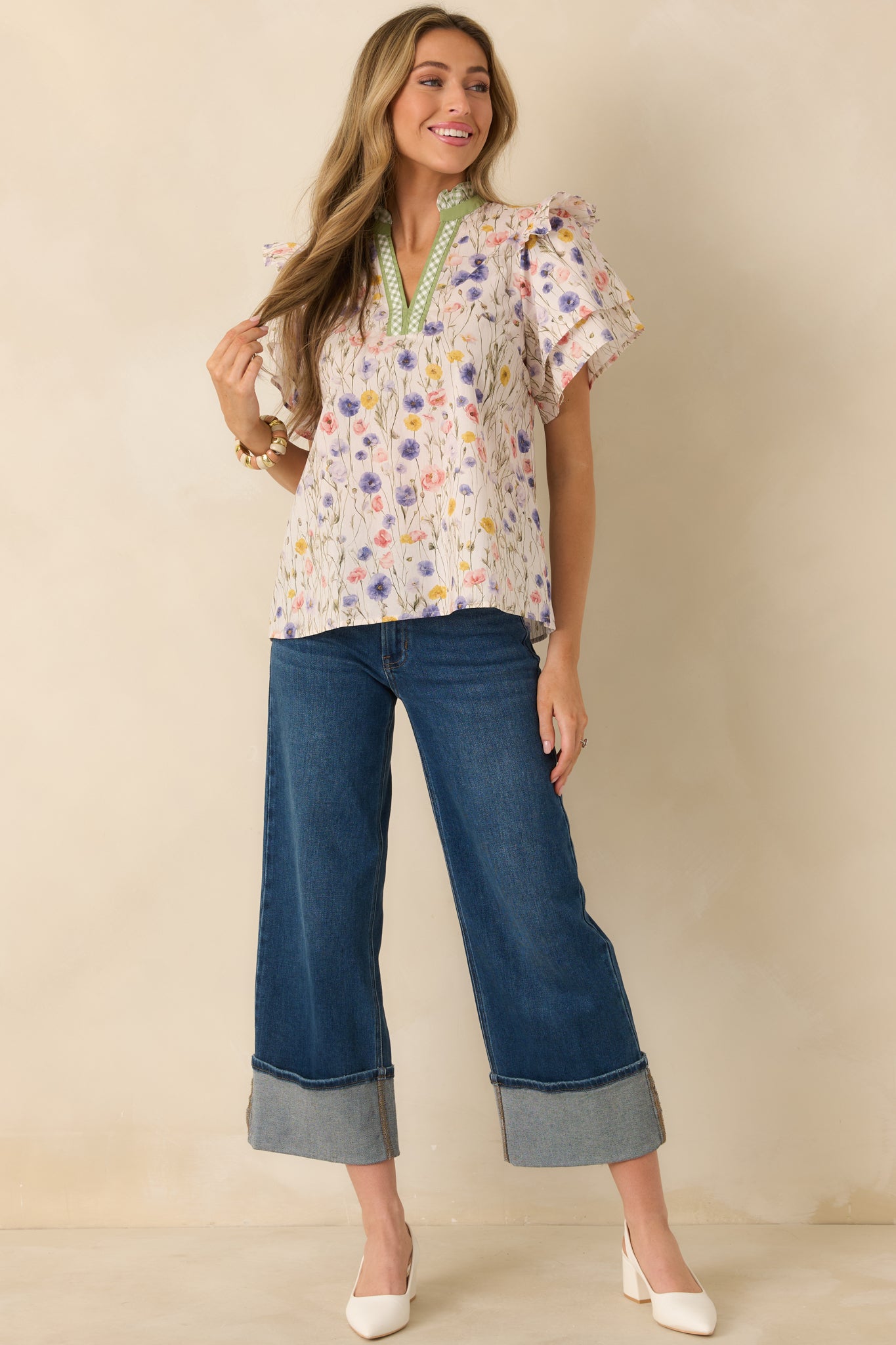 Ivory blouse with a green-trimmed neckline and ruffled cap sleeves, made from breathable woven cotton.