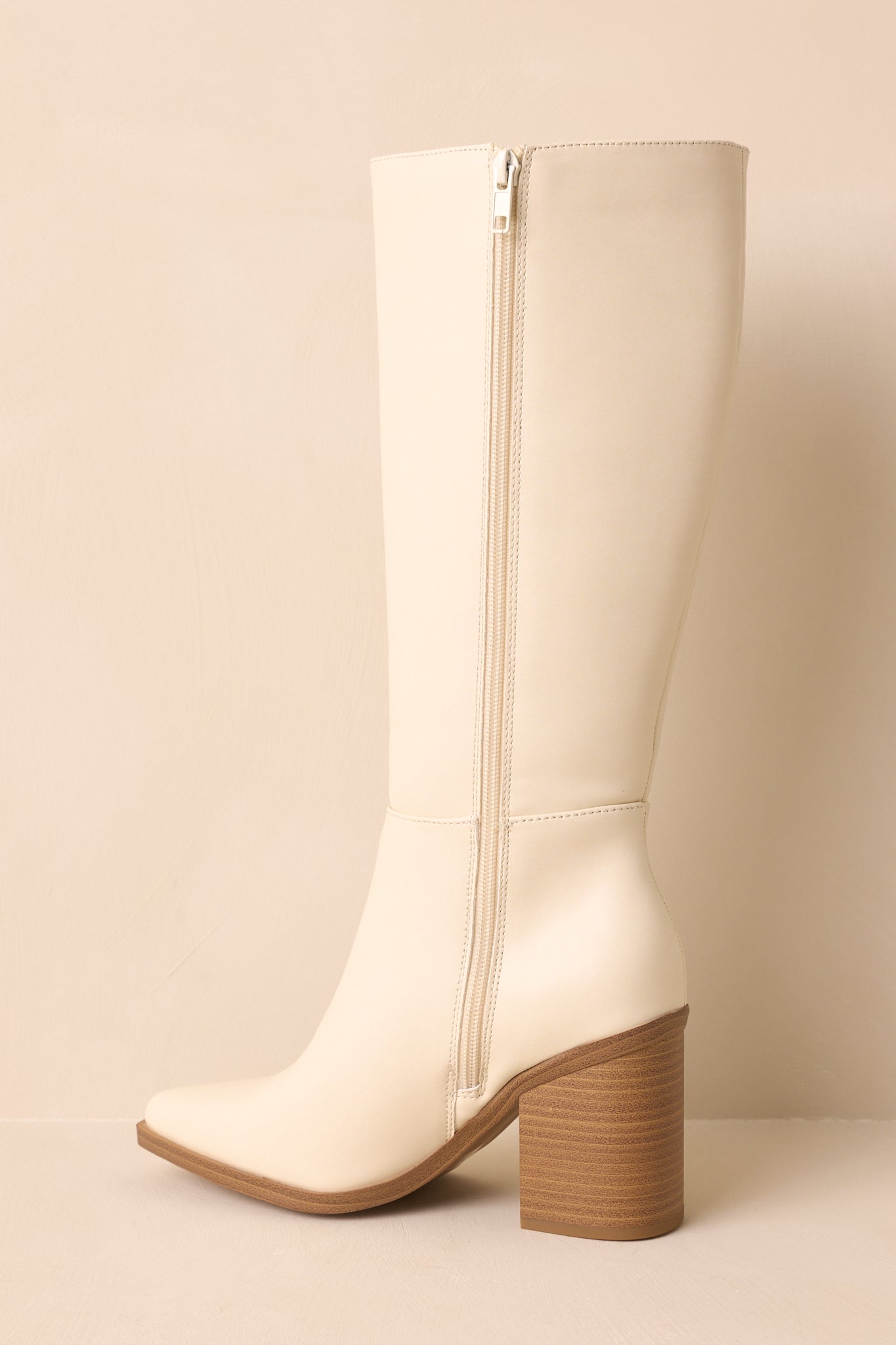 A back angled view of the ivory boots on a beige background, emphasizing the stacked block heel.