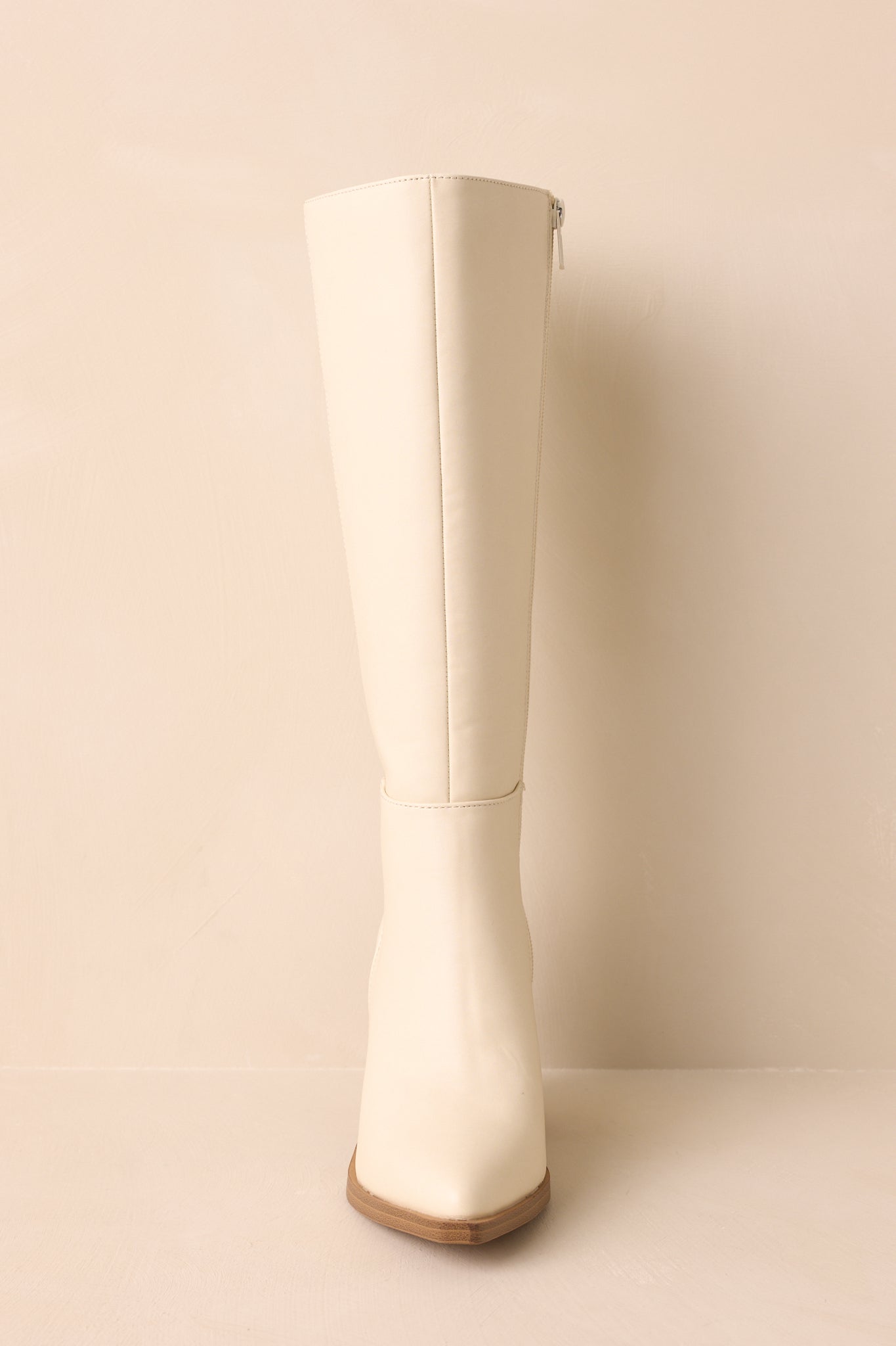 A straight-on front view of the ivory boots capturing the pointed toe and stitched paneling.