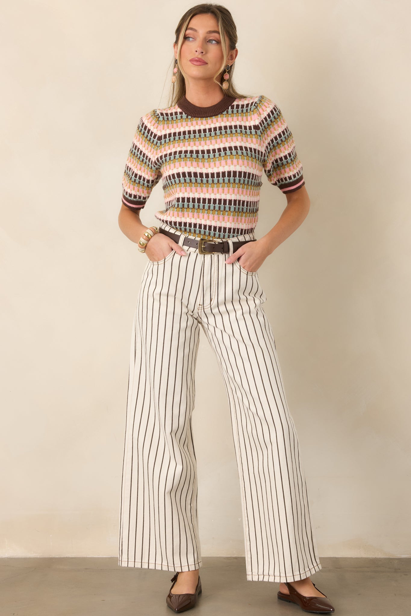 Ivory 100% cotton denim pants with vertical brown pinstripes, a high-rise waist, traditional five-pocket styling, and relaxed full-length wide legs.