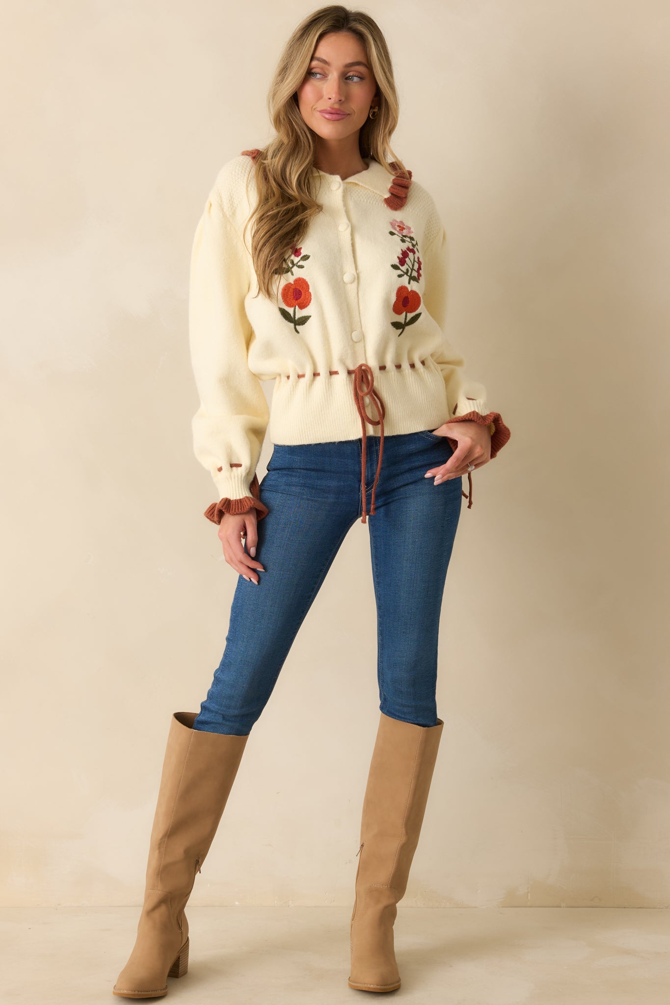 Ivory button-up cardigan with long puff sleeves, rust tie cuffs, ruffle trim collar, and floral front embroidery.