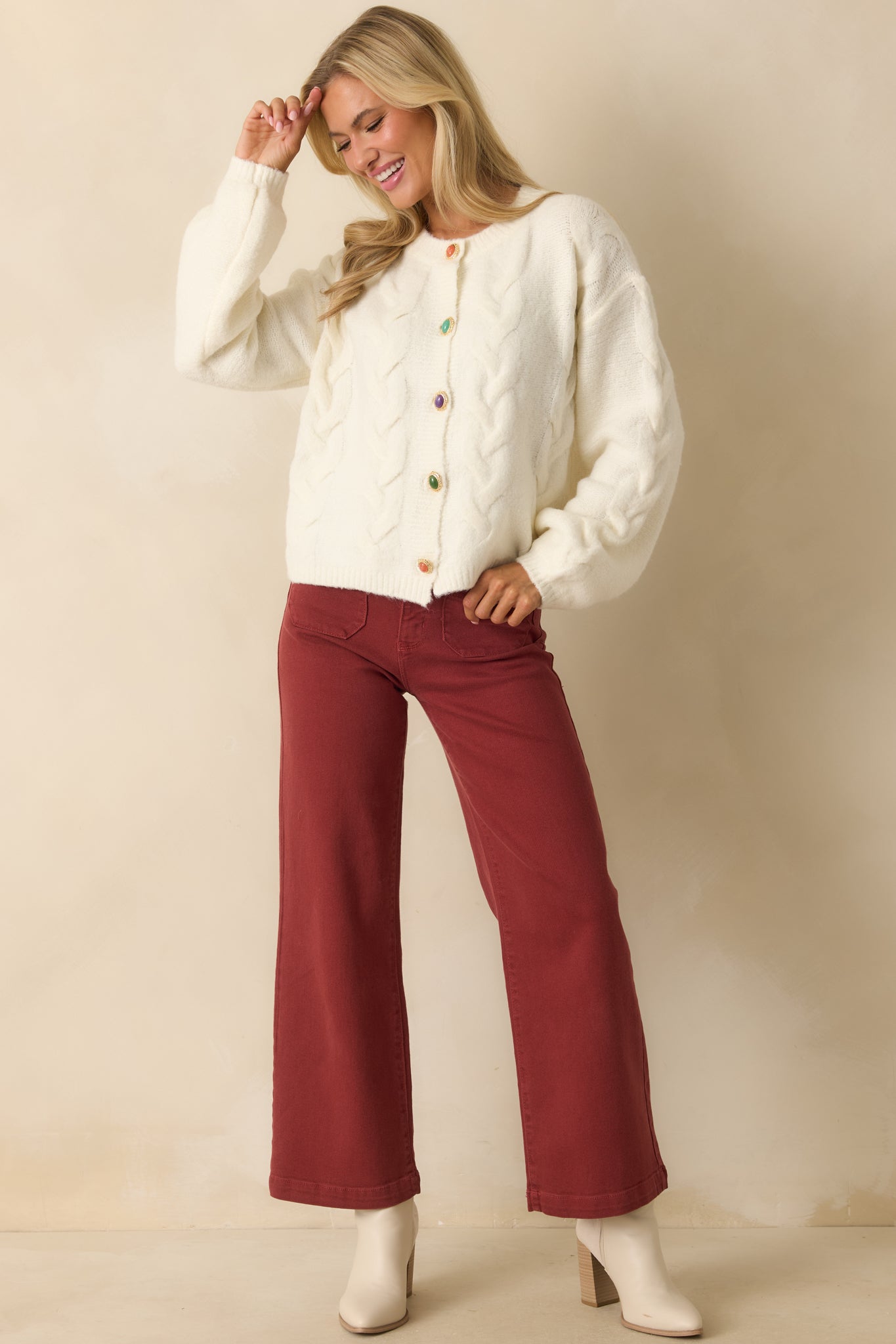 Ivory cable knit cardigan with long sleeves, ribbed trim, and colorful button detailing in a relaxed fit.