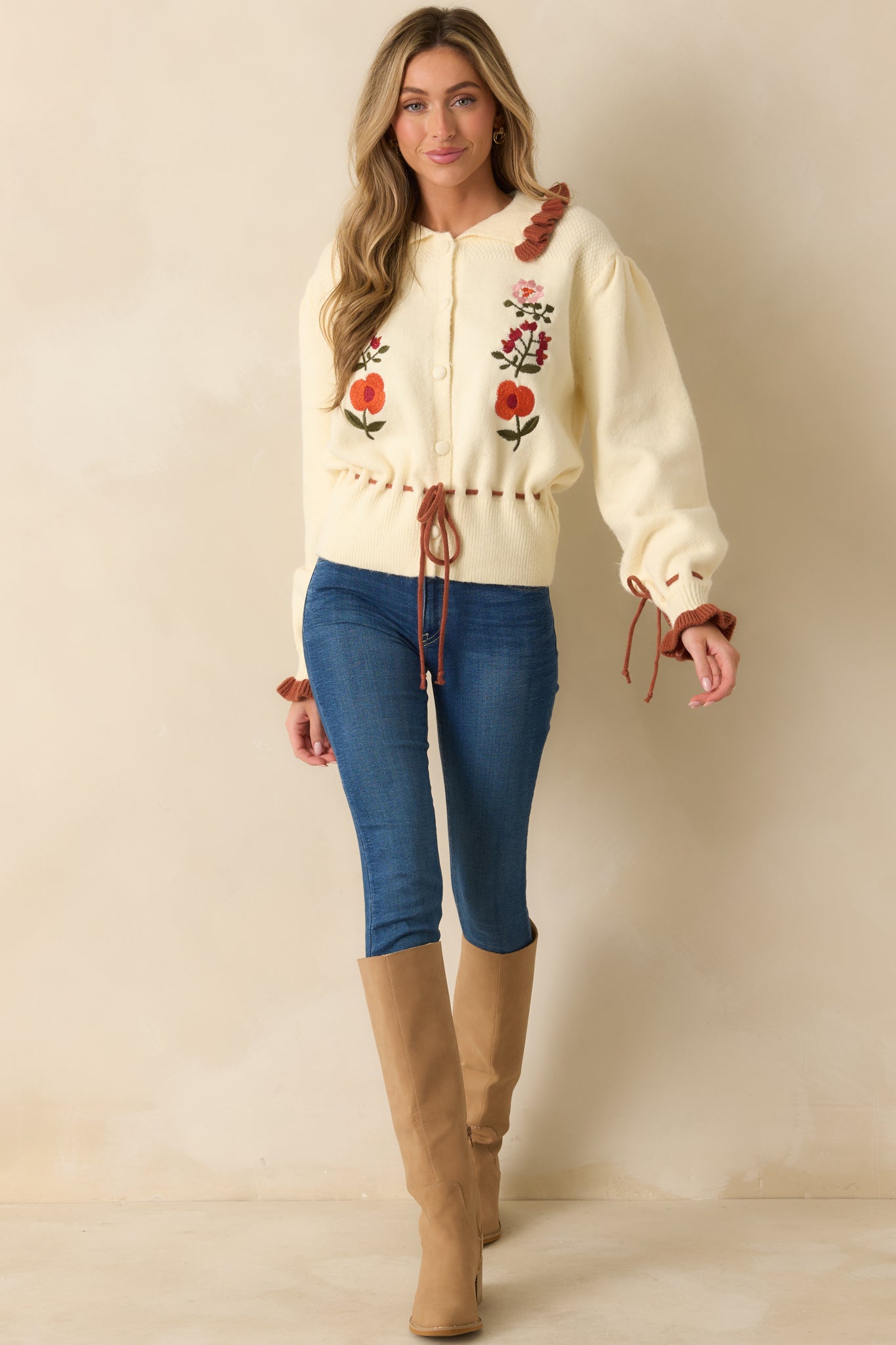 Front-facing ivory cardigan with puff sleeves, rust ruffle collar and tie cuffs, drawstring waist, and floral embroidery for a vintage-inspired look.