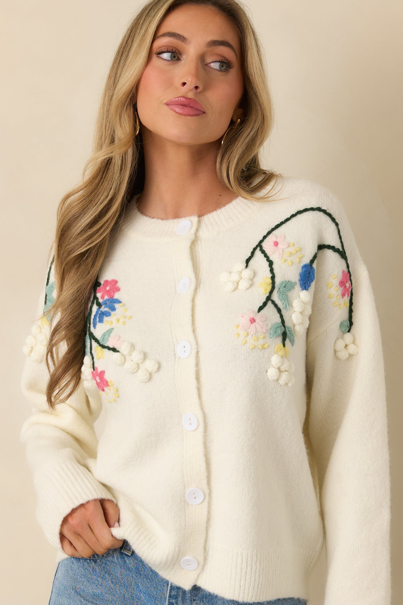 Relaxed ivory cardigan featuring floral-embroidered accents, long sleeves, and a smooth knit finish.