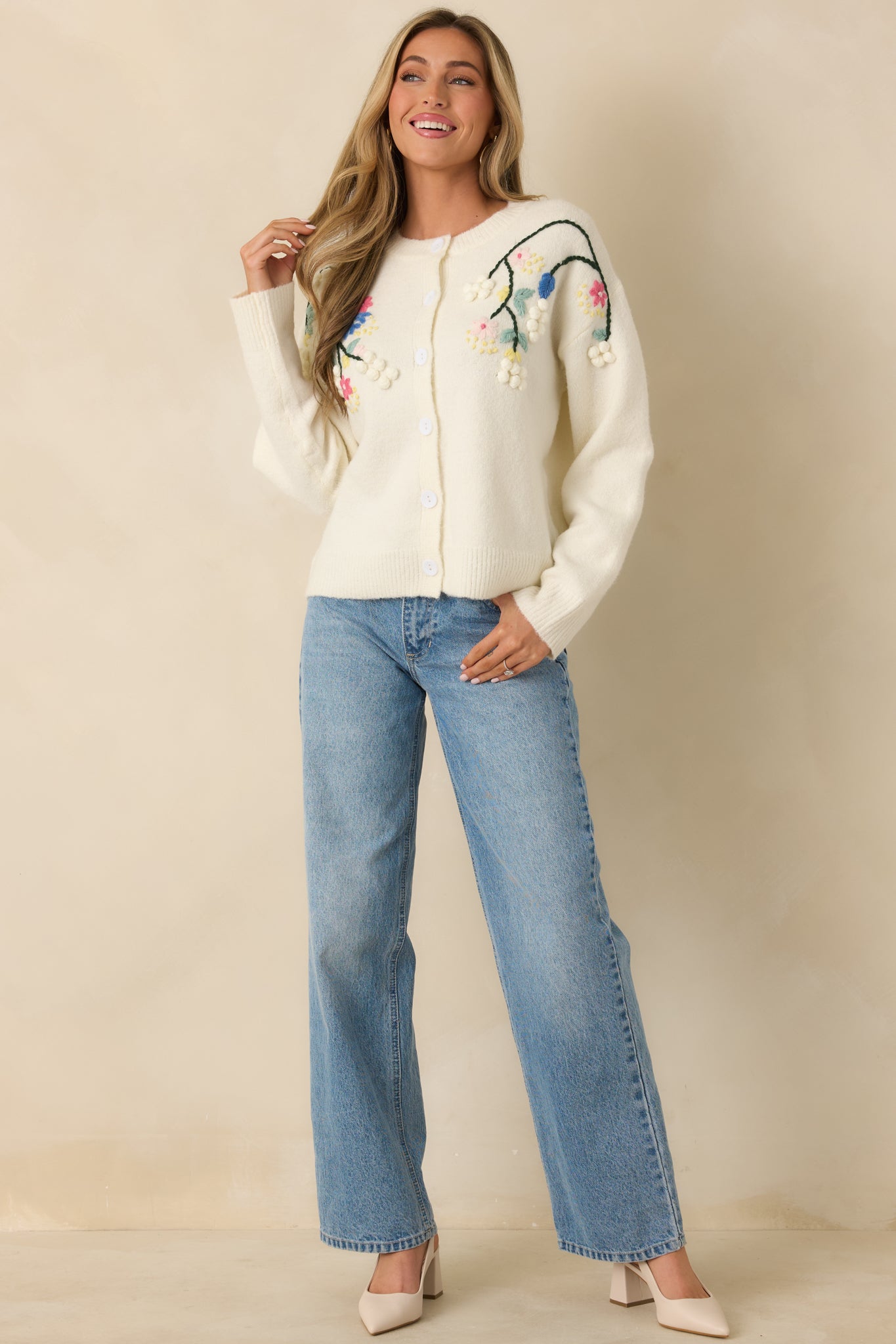Soft ivory cardigan featuring a button-front closure and colorful floral embroidery across the shoulders and upper bodice.