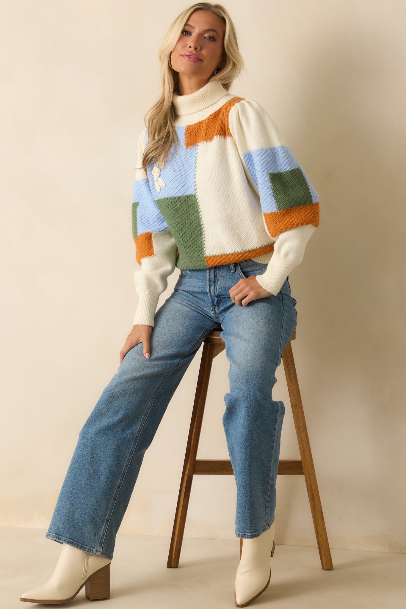 Ivory colorblock sweater featuring green, blue, and rust knit panels with a ribbed fold-over turtleneck and puff long sleeves.