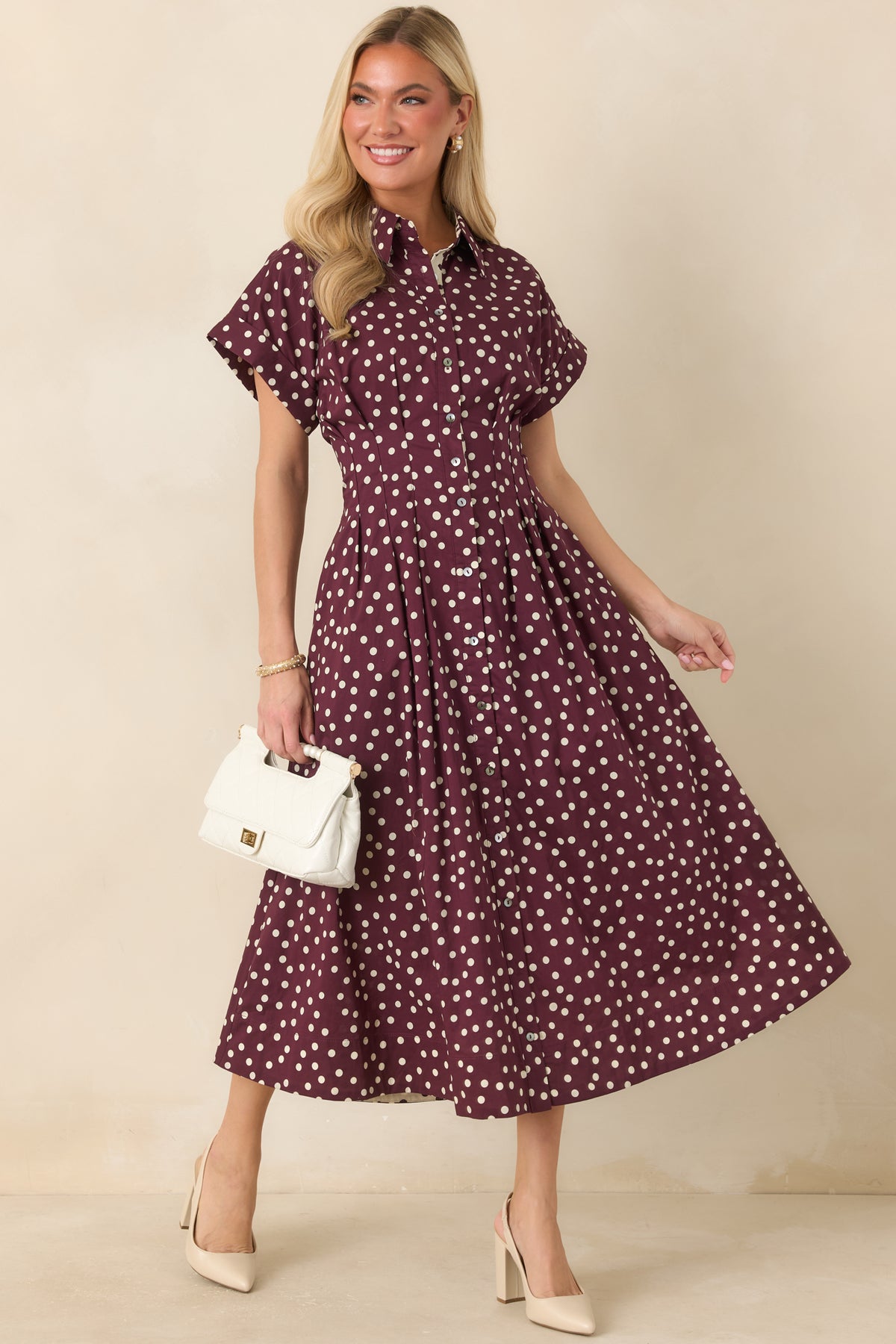 Ivory cotton midi dress with plum polka dots, a collared button-front bodice, tailored waist seams, short sleeves, and flowing skirt.