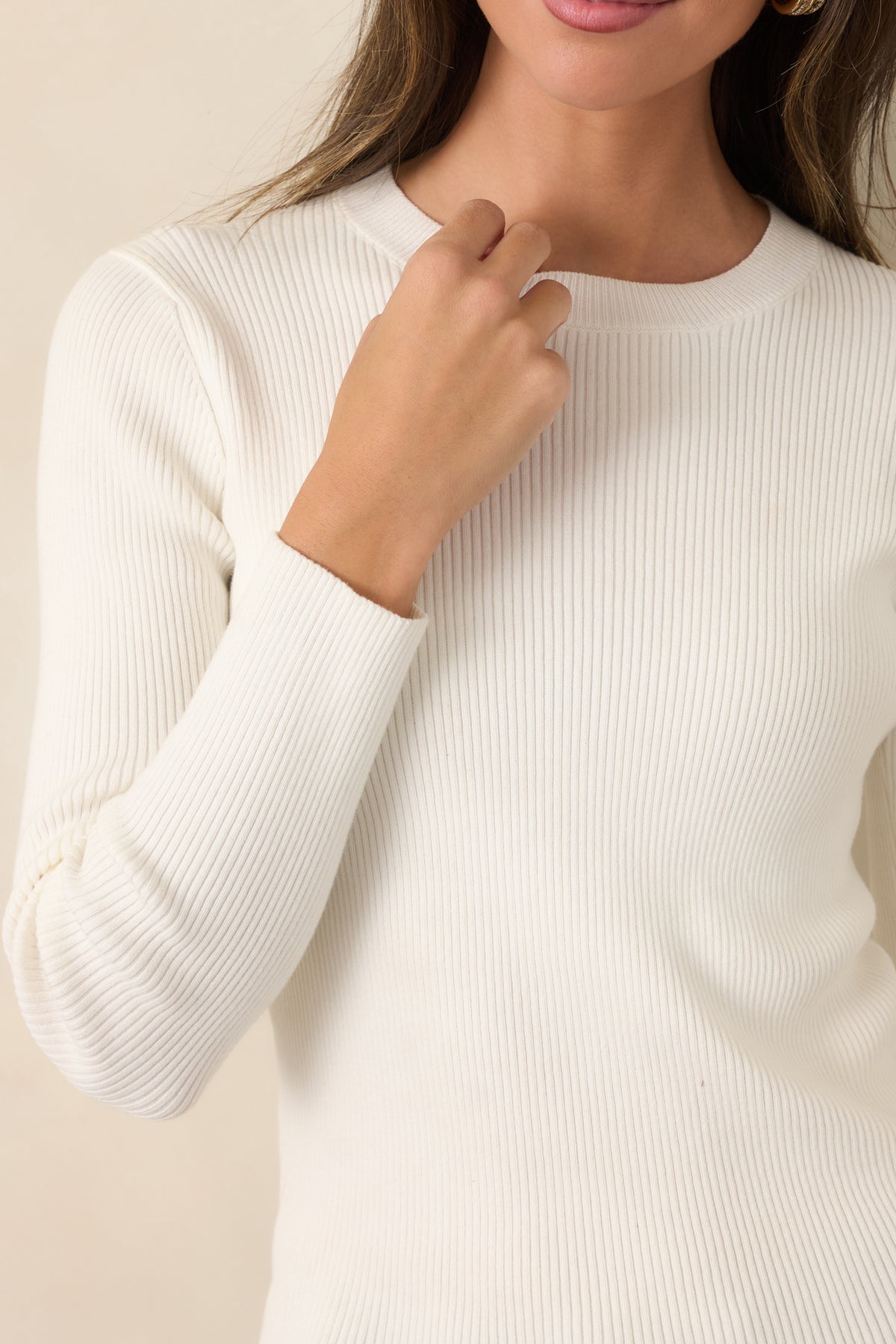 Close-up of ivory cotton knit top showcasing fine vertical ribbing, a ribbed crew neckline, and fitted long sleeves.