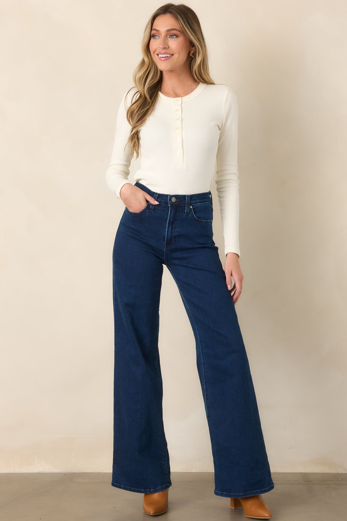 Ivory long-sleeve top featuring a rounded scoop neckline, buttoned Henley placket, close-to-body fit, and neat cropped hem.